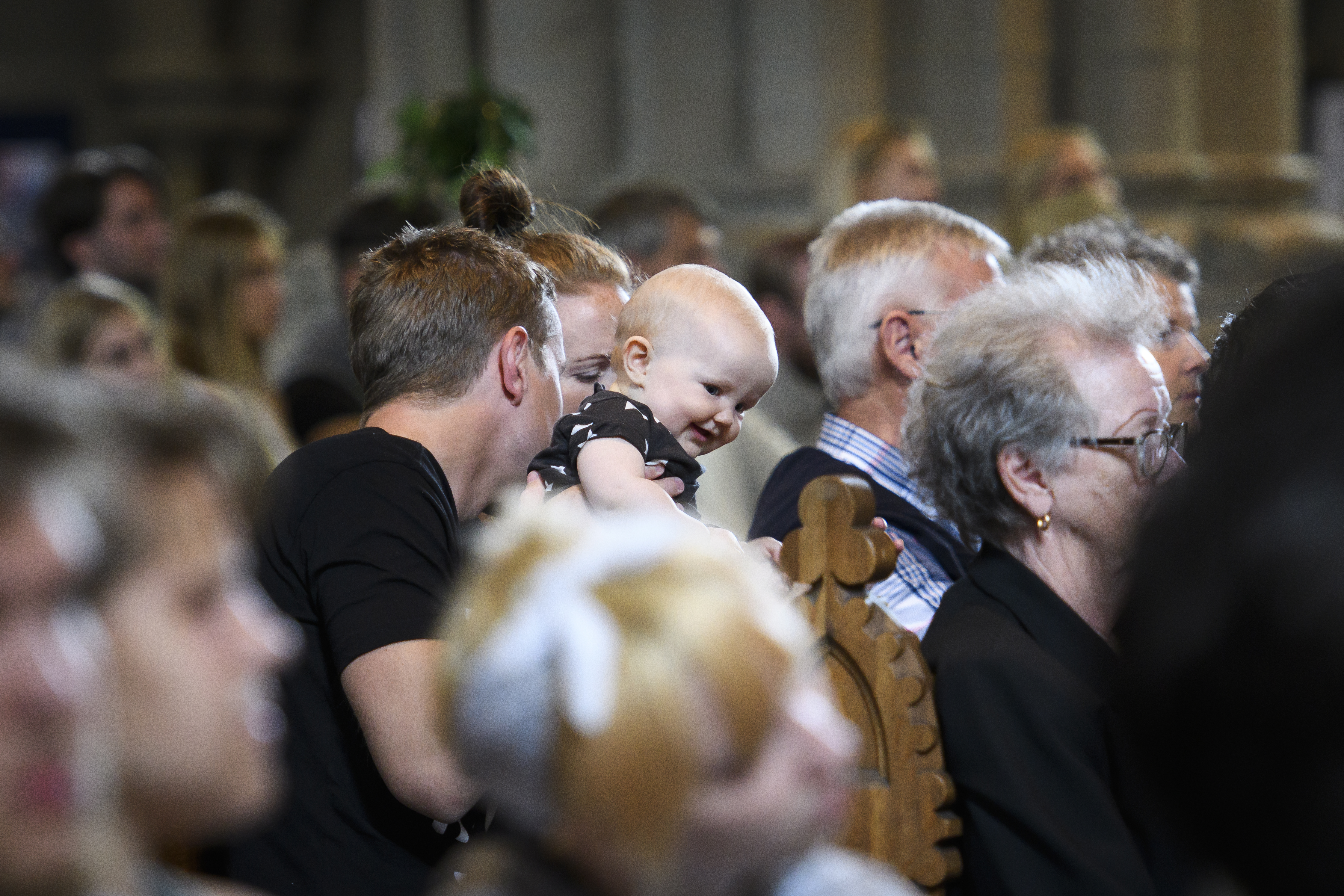 En man håller ett litet barn. barnet ler mitt bland människorna som sitter i kyrkbänkarna.