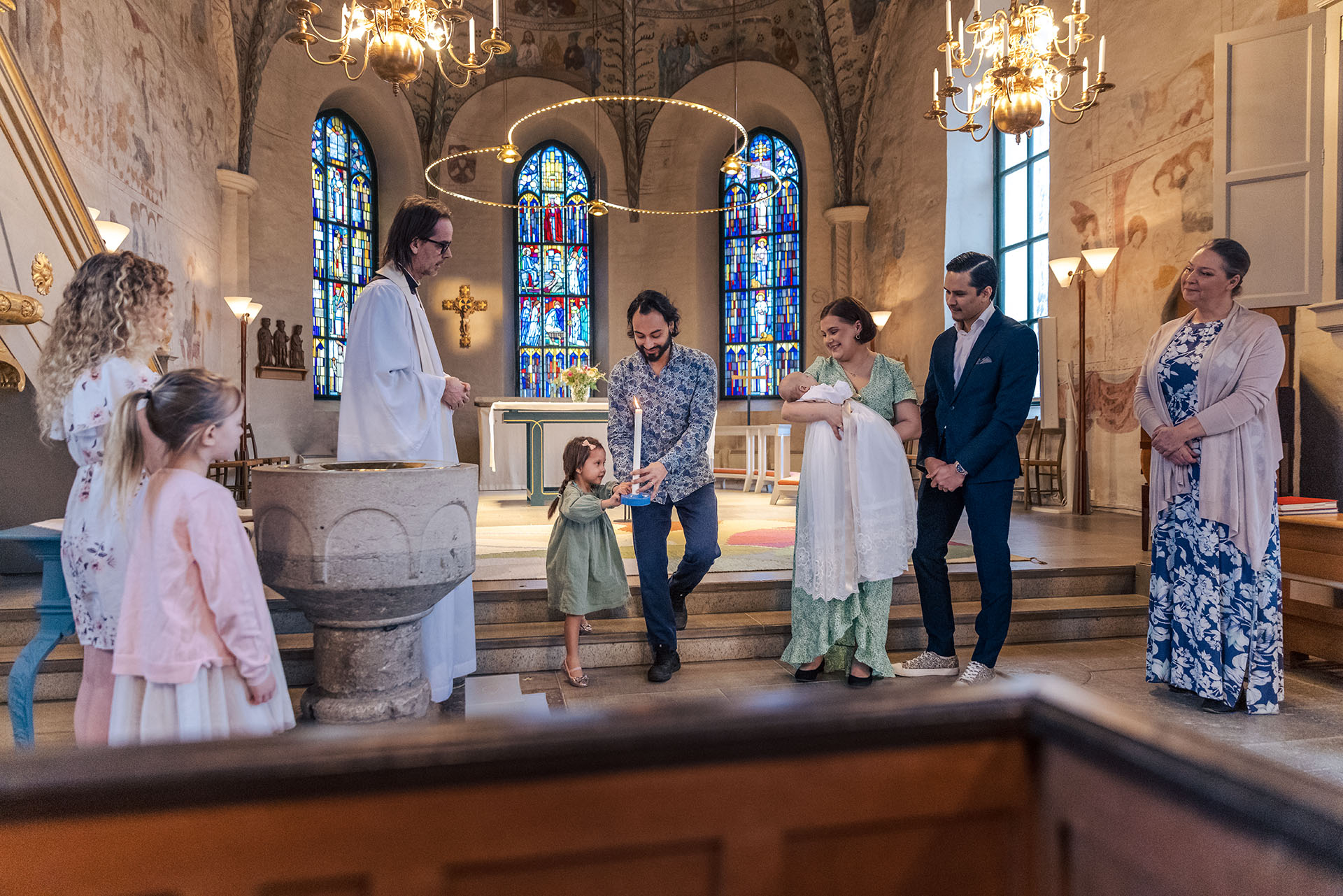 En glad dopfamilj, faddrar och präst står långt fram i kyrkan.