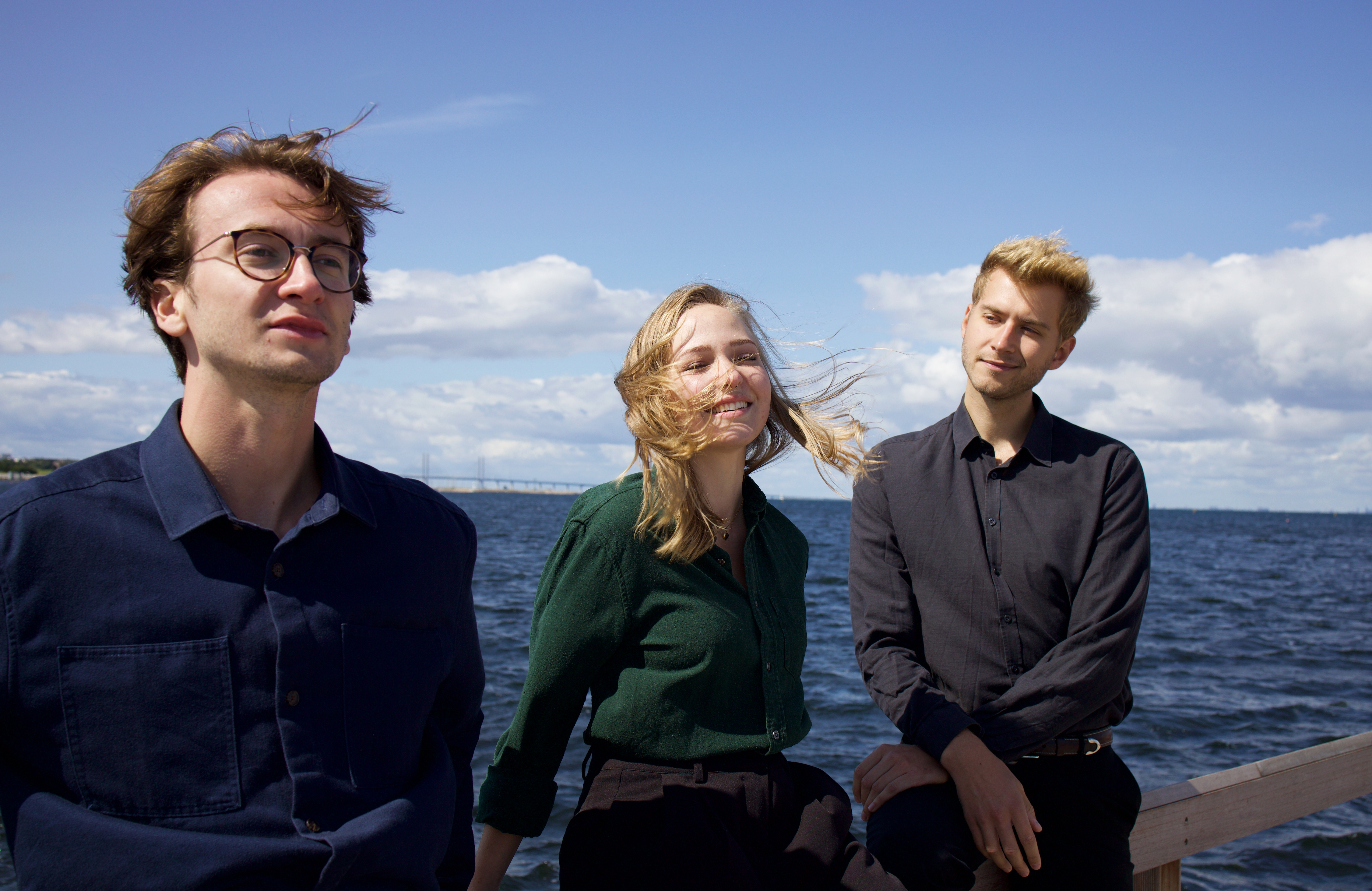Tre personer vid havet. Himlen är blå.