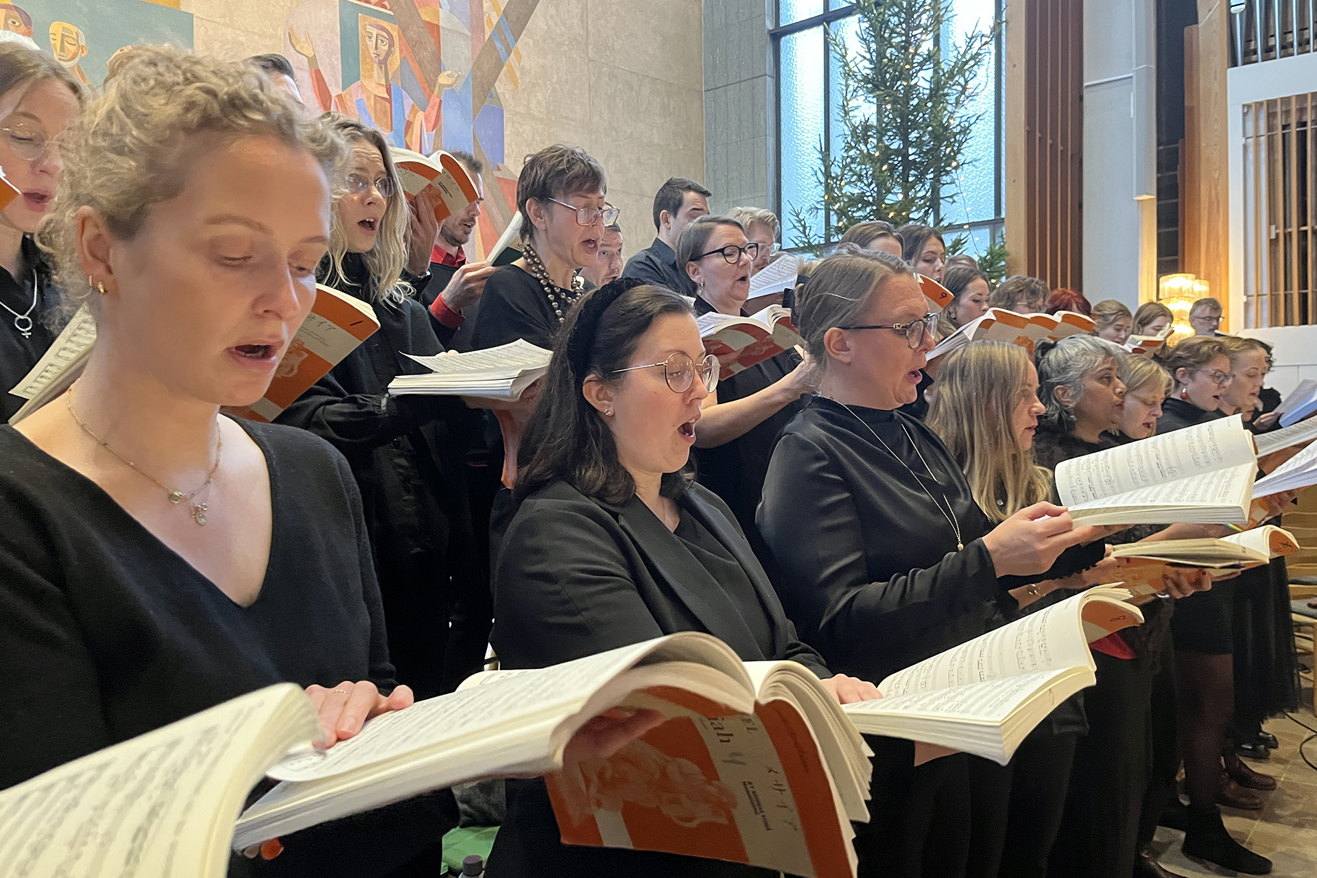 Människor sjunger och har nothäfte uppslagna i händerna.