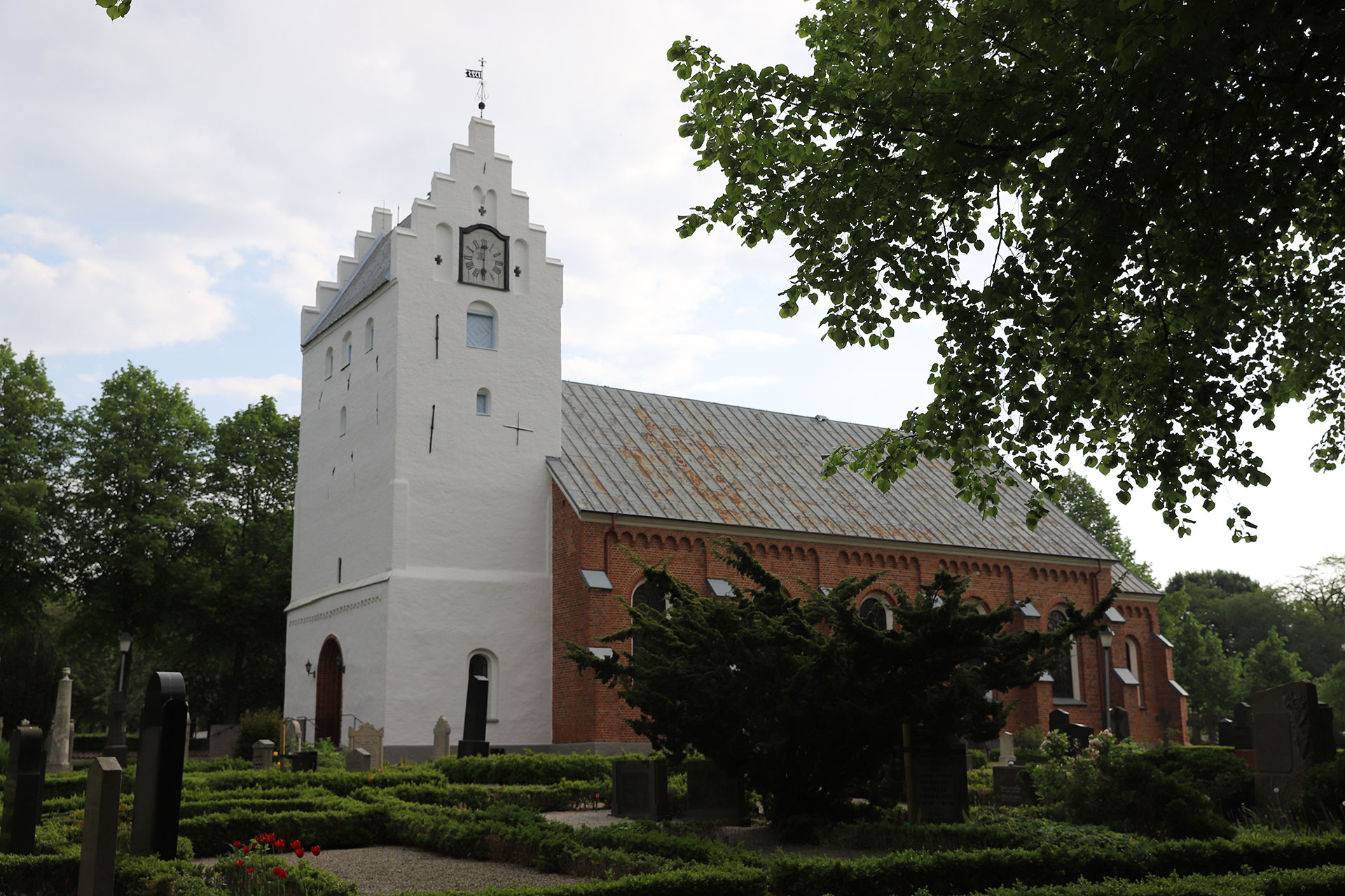 Vitt kyrktorn och ett huvudskepp i rött tegel.