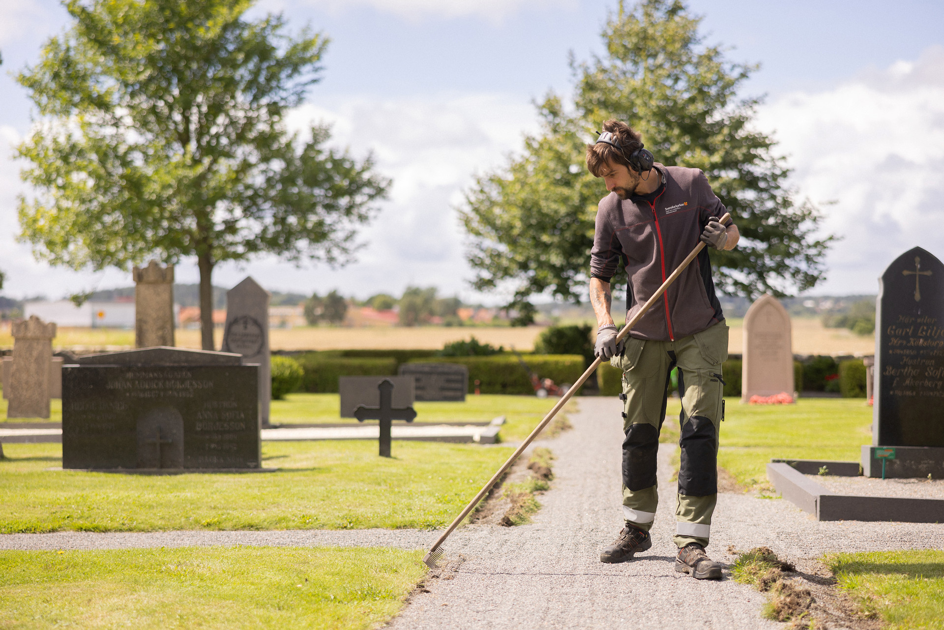 En vaktmästare som krattar en grusgång på en kyrkogård. 