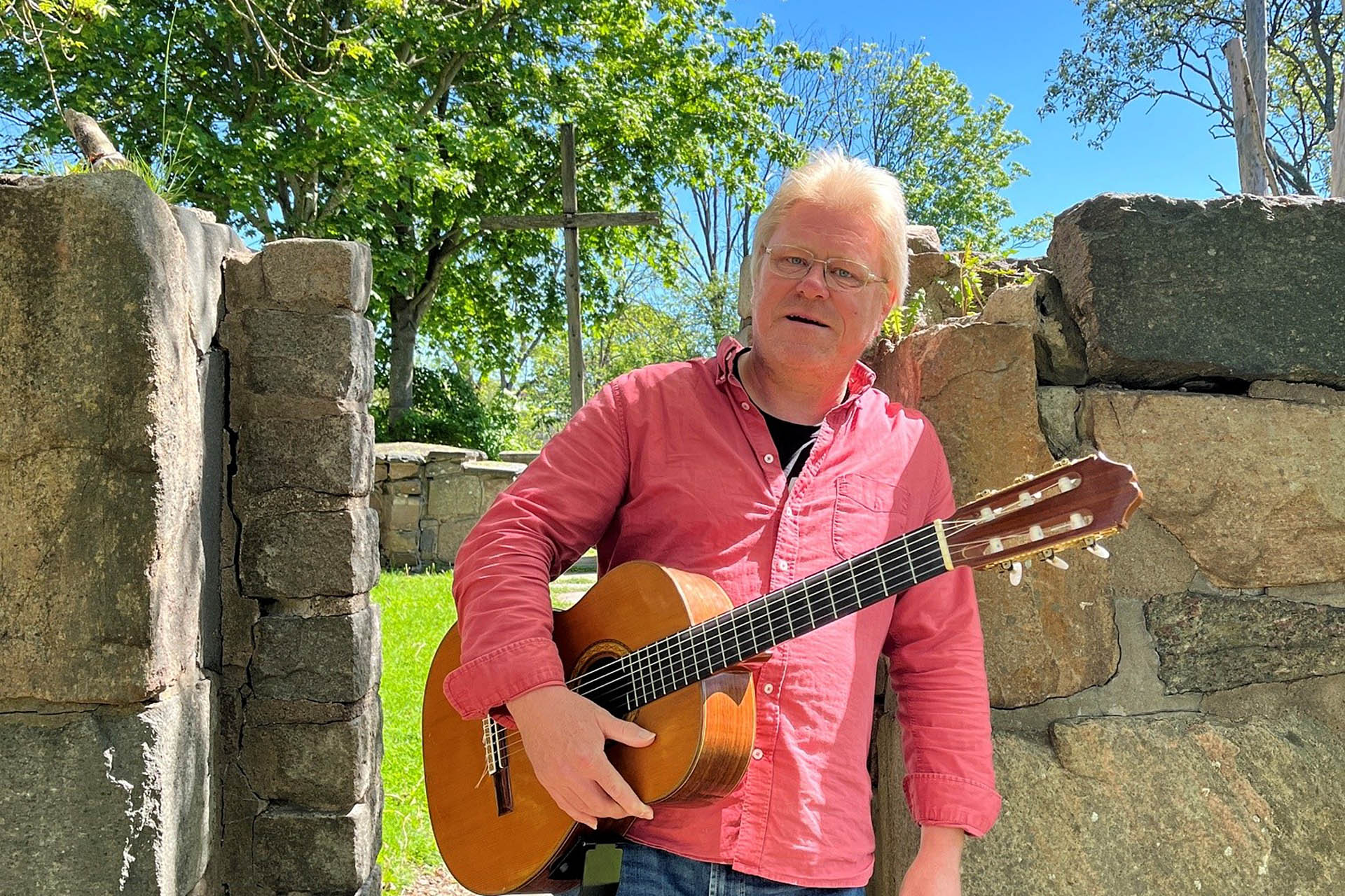En man med gitarr står vid en ruin.