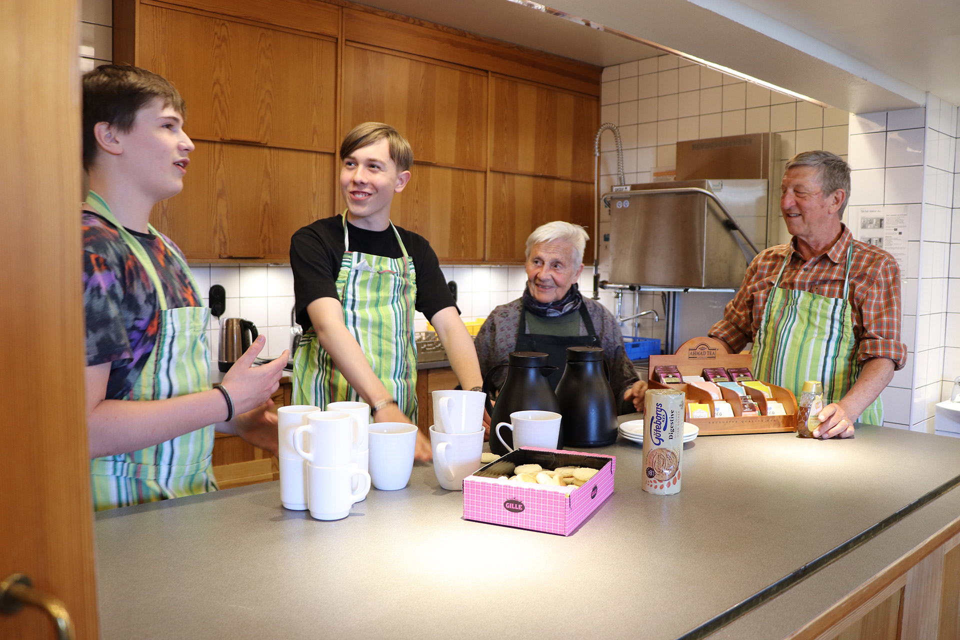 Fyra personer i olika åldrar står i köket och plockar fram koppar.