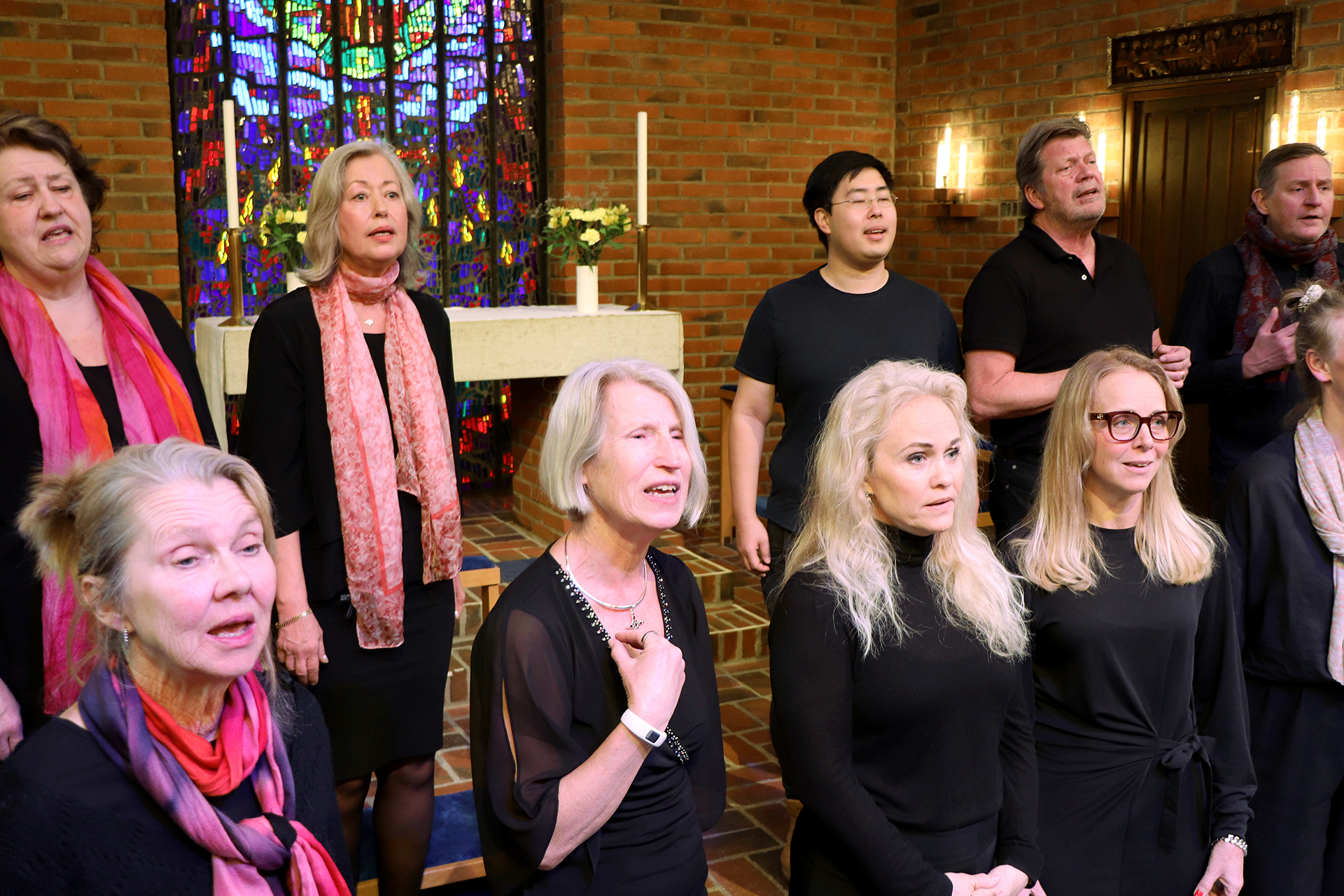 Personer i svart och rosa sjunger, i mitten finns en plats ledig.