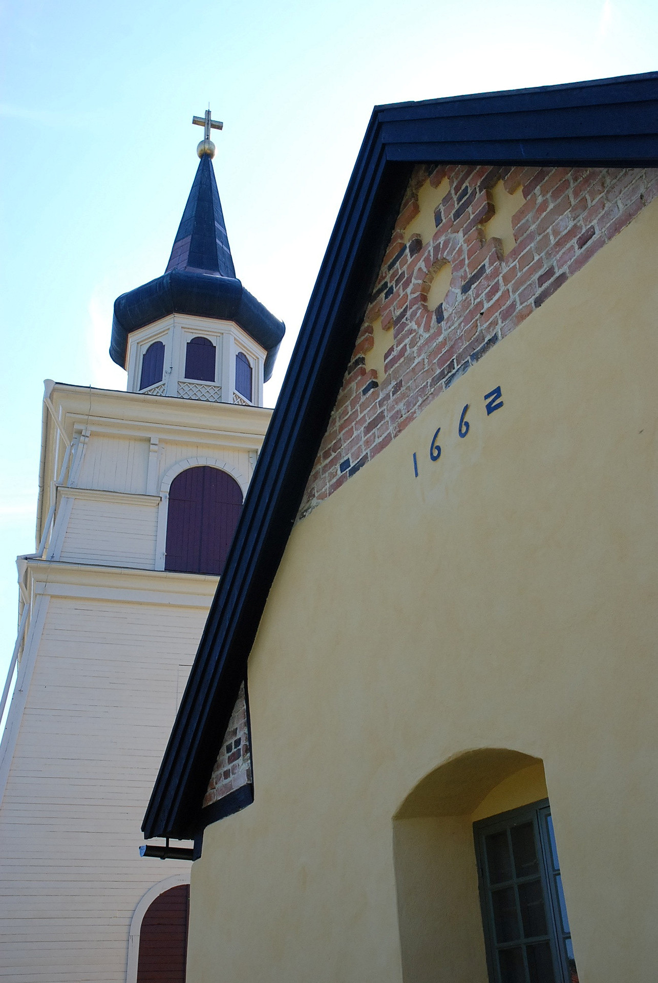 En gulputsad gavel på en kyrka. På gaveln står det 1662. I bakgrunden skymtar en klockstapel.