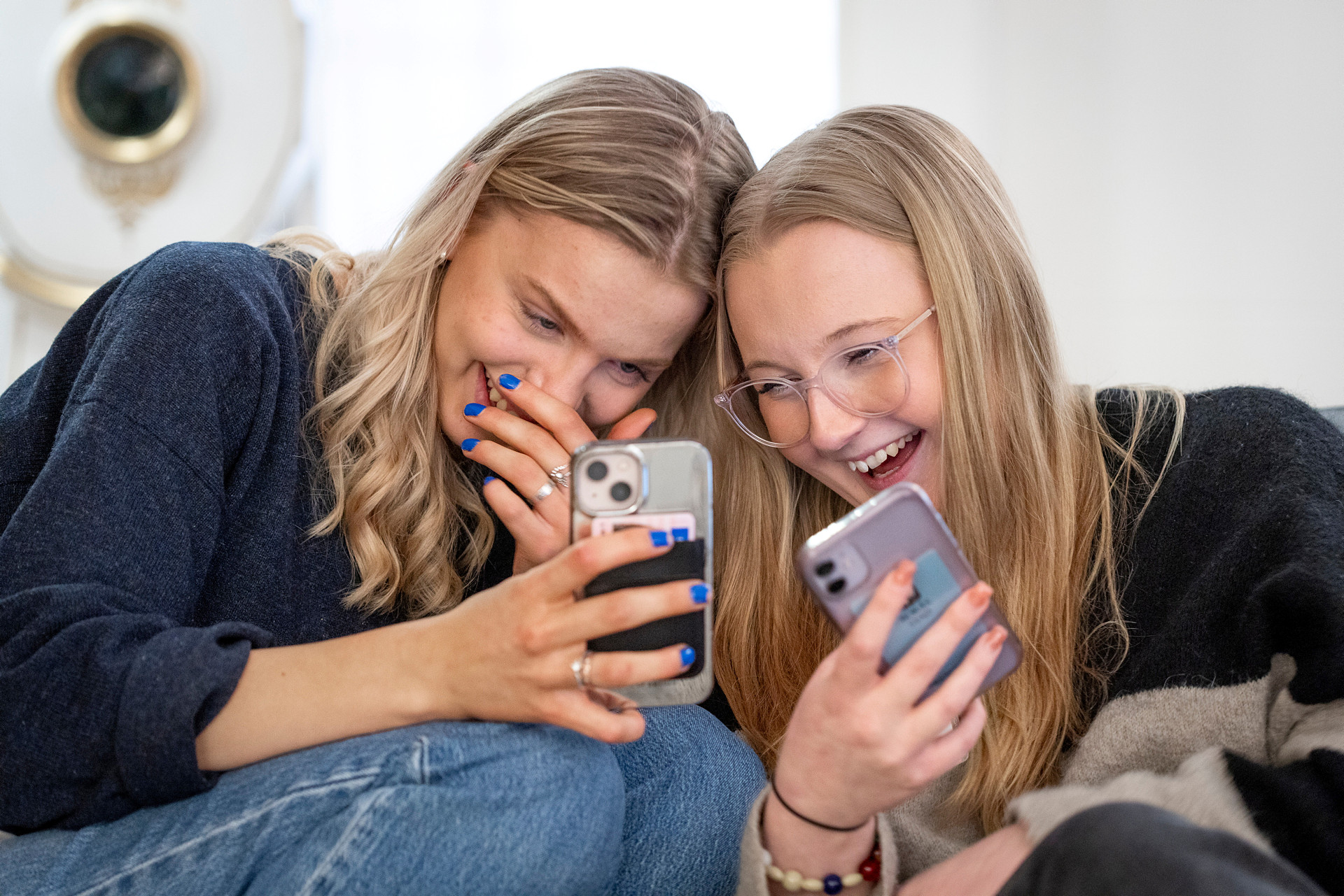 Två unga tjejer skrattar tillsammans medan de tittar på varandras mobiltelefoner.