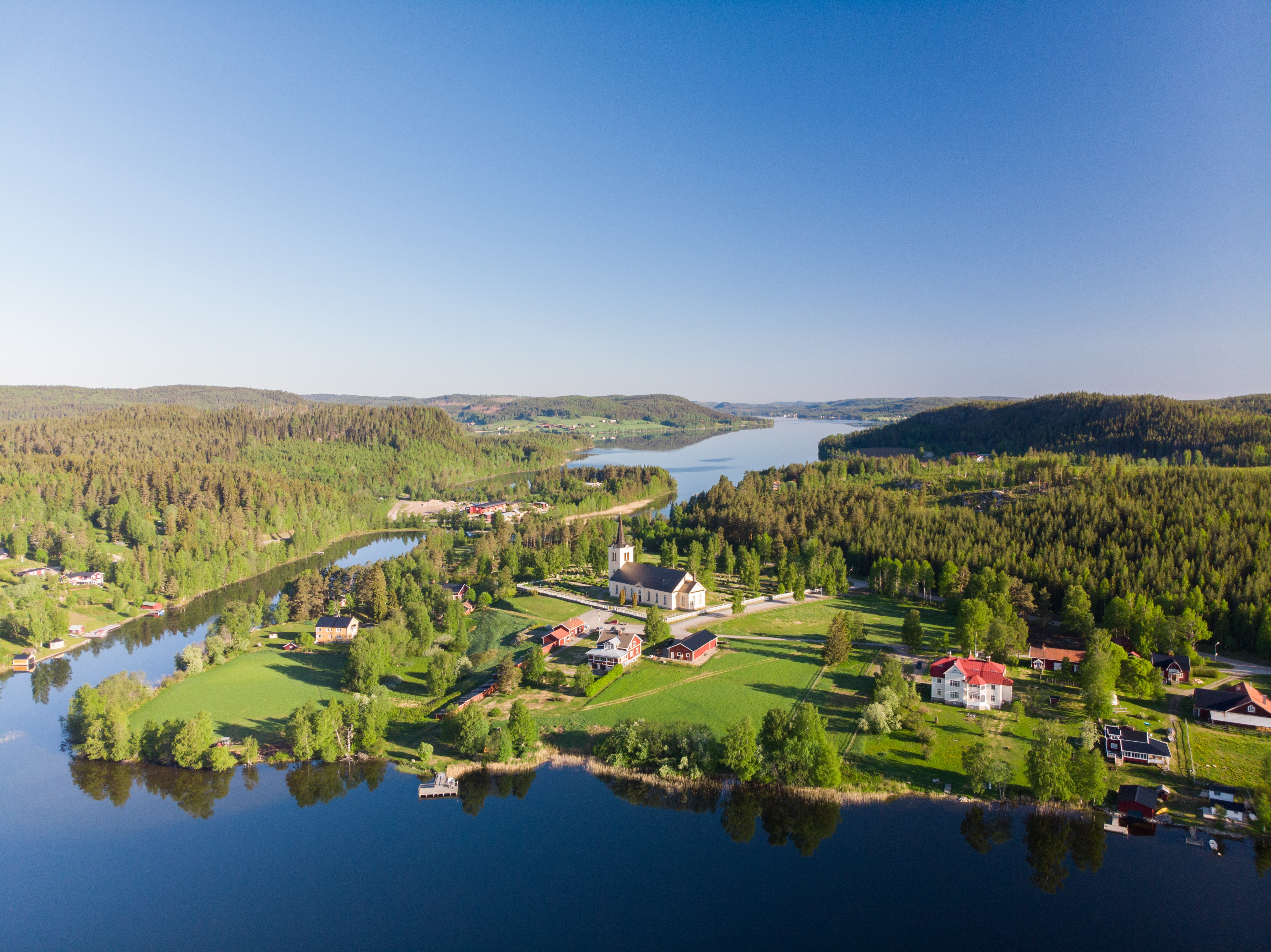En drönarbild av en bygd där man ser en sjö, hus och en kyrka.