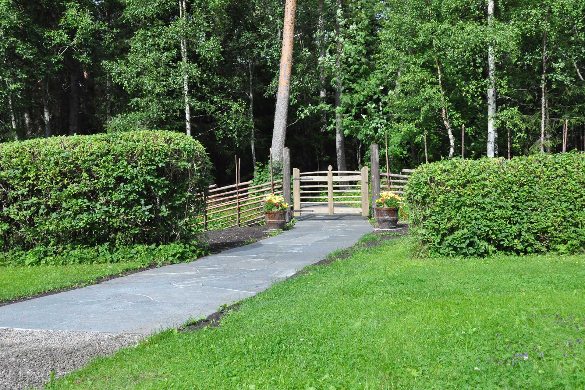 Trästaket med grind avgränsar Näs kyrkogård och askgravlunden i skogskanten.