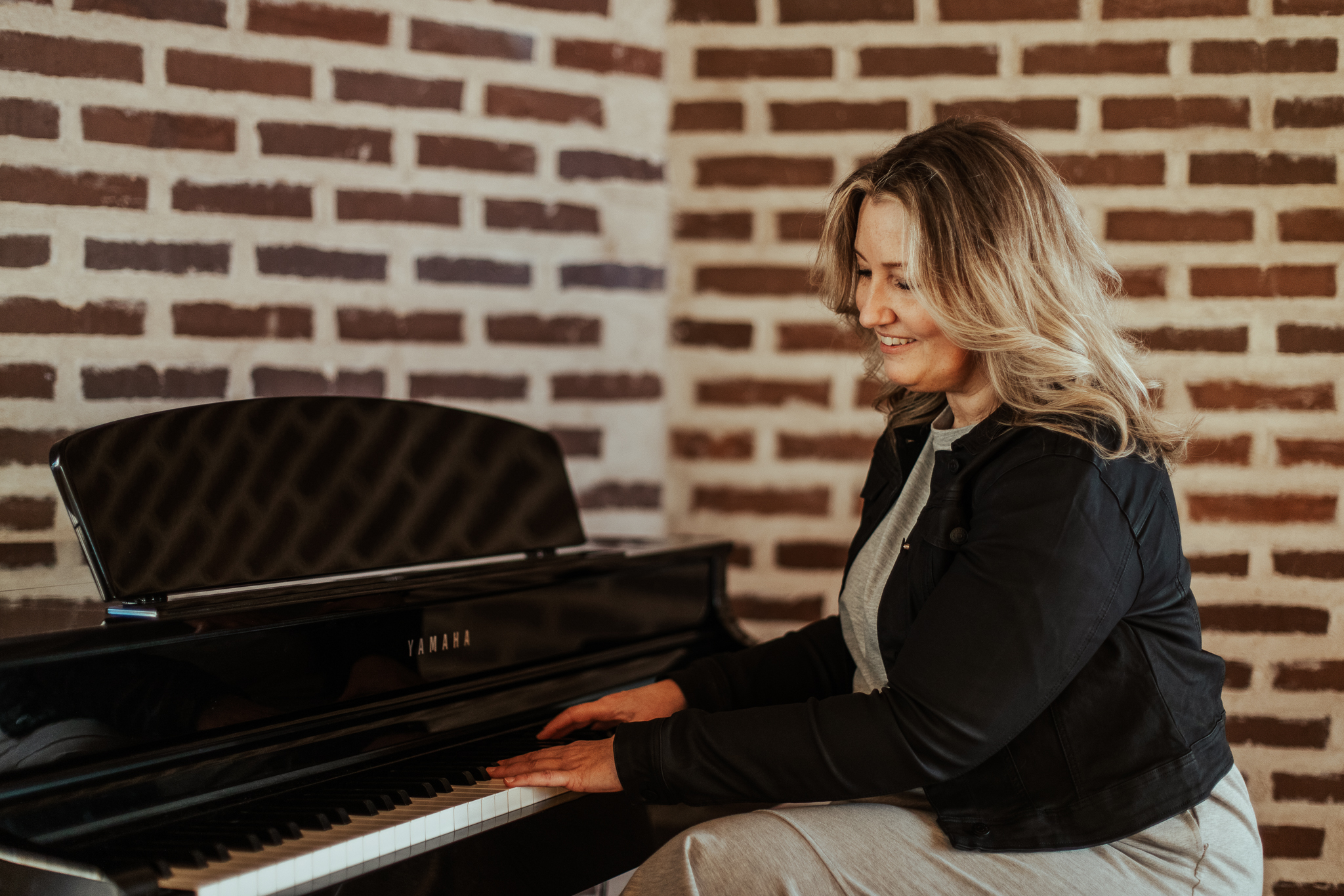 Kvinna med långt, blont hår som sitter vid ett piano och spelar.