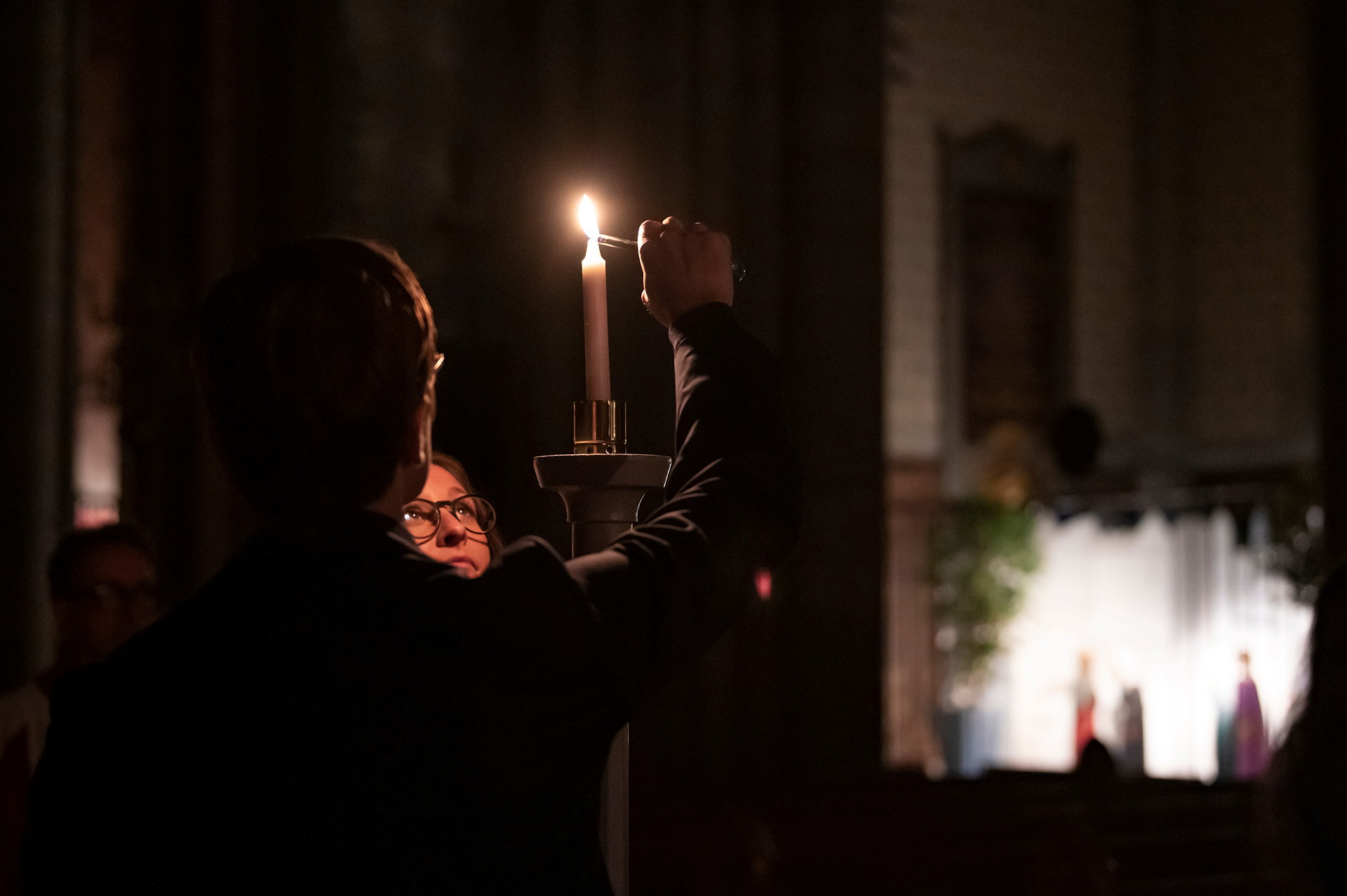 Tre personer står i dunklet och tänder tillsammans en ljushållare som lyser upp i Uppsala domkyrkas mörker.