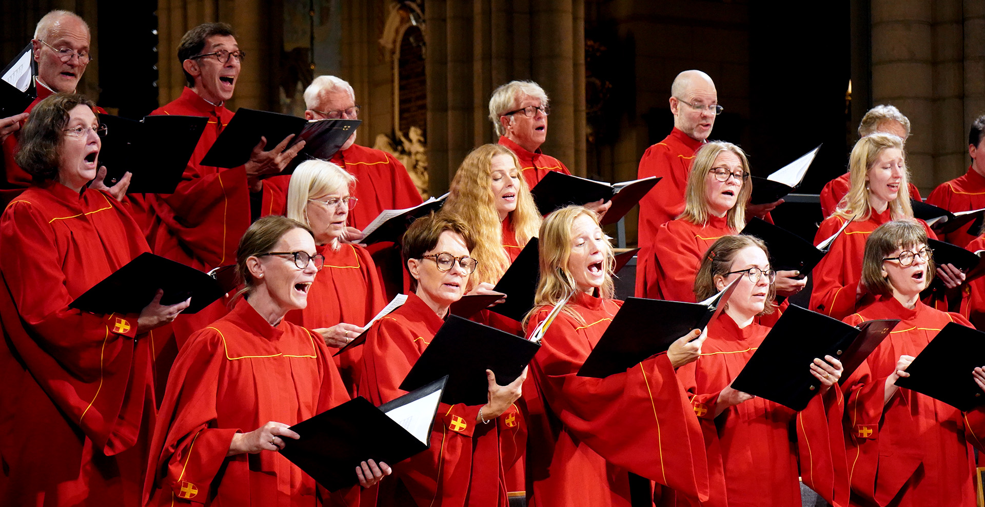 Uppsala domkyrkokör i röda kåpor i full sångglädje framme i domkyrkans korsmitt.