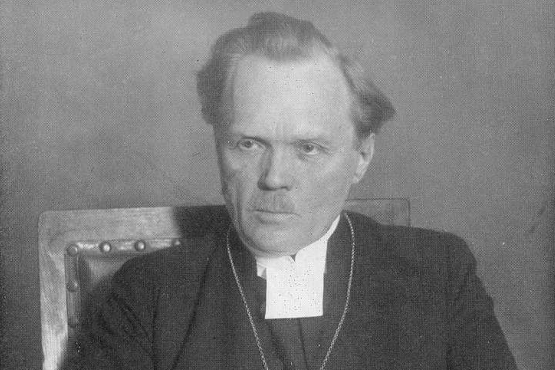 Svartvitt foto av en medelålders man med allvarlig uppsyn. Runt halsen har han en prästkrage.