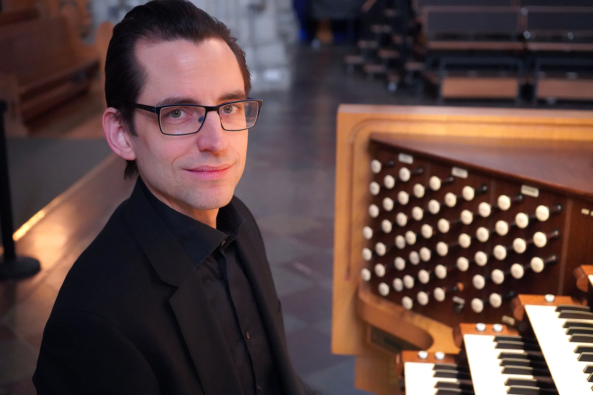 Porträtt på Pontus Leitz i glasögon och svart kavaj viod Ruffattiorgelns spelbord i Uppsala domkyrka.