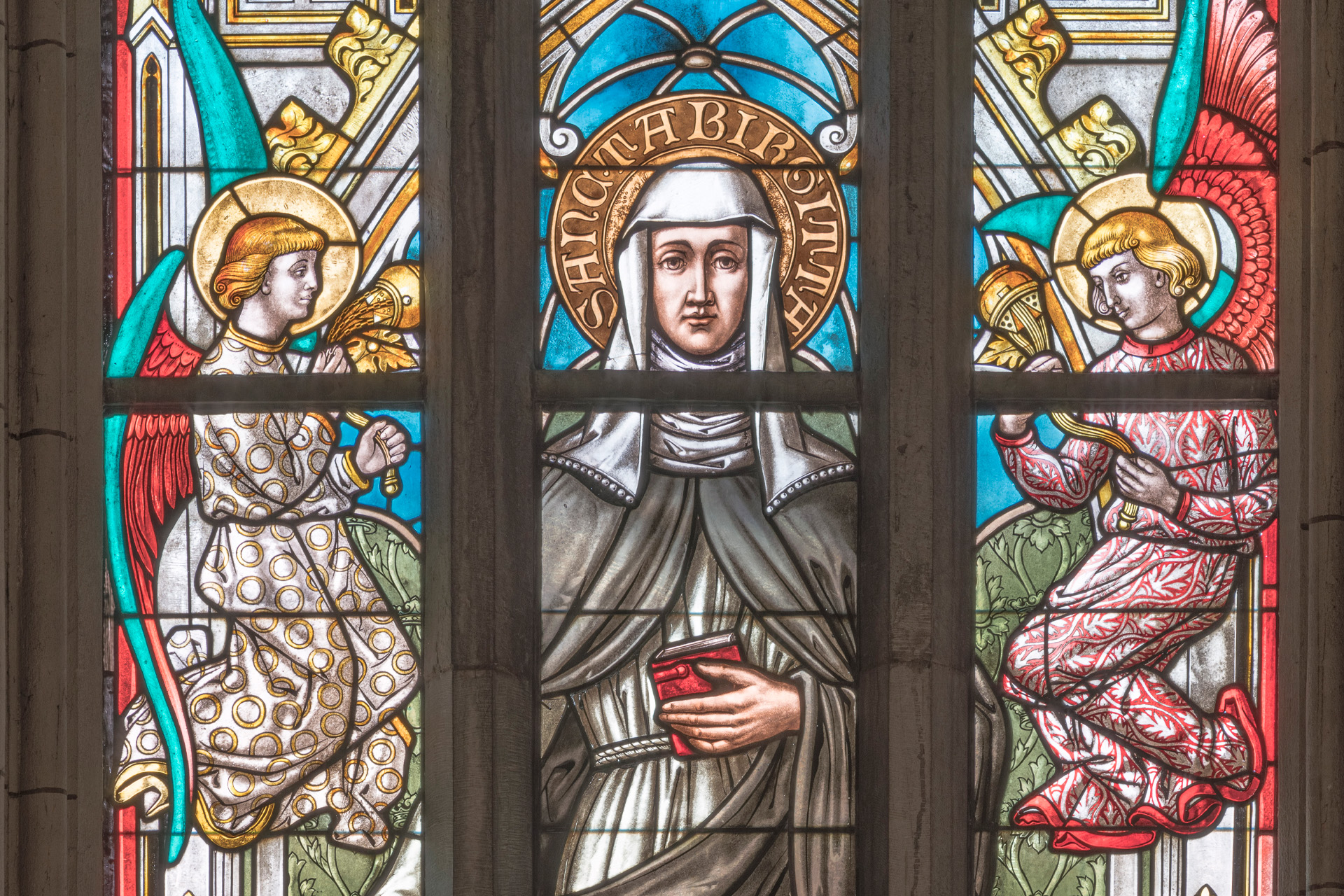 Del av ett kyrkfönster föreställande ett kvinnligt helgon med en ängel på vardera sida.