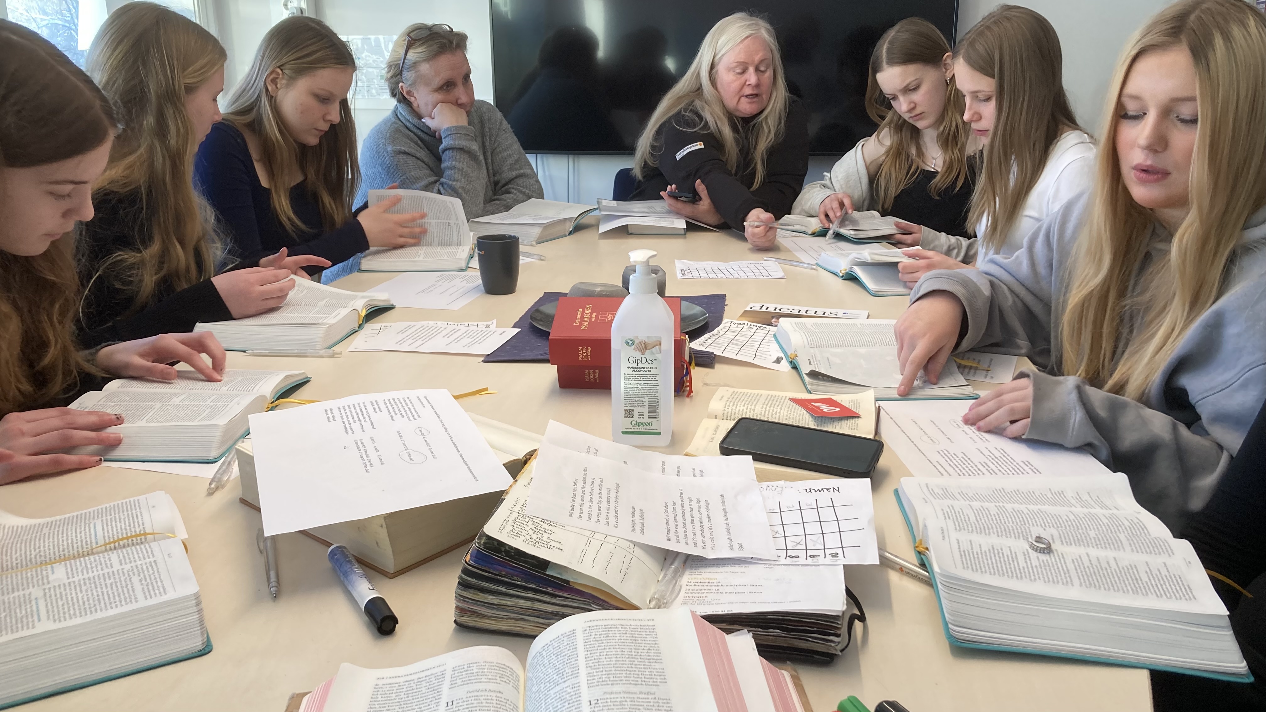 En grupp konfirmander med ledare samlade runt ett bord för att läsa Bibeln
