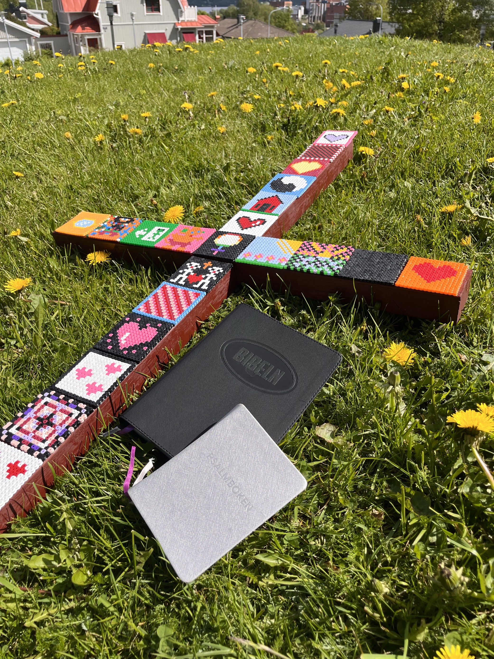 Ett stort processionskord prytt av pärlplattor ligger i gräset tillsammans med en bibel och psalmbok.