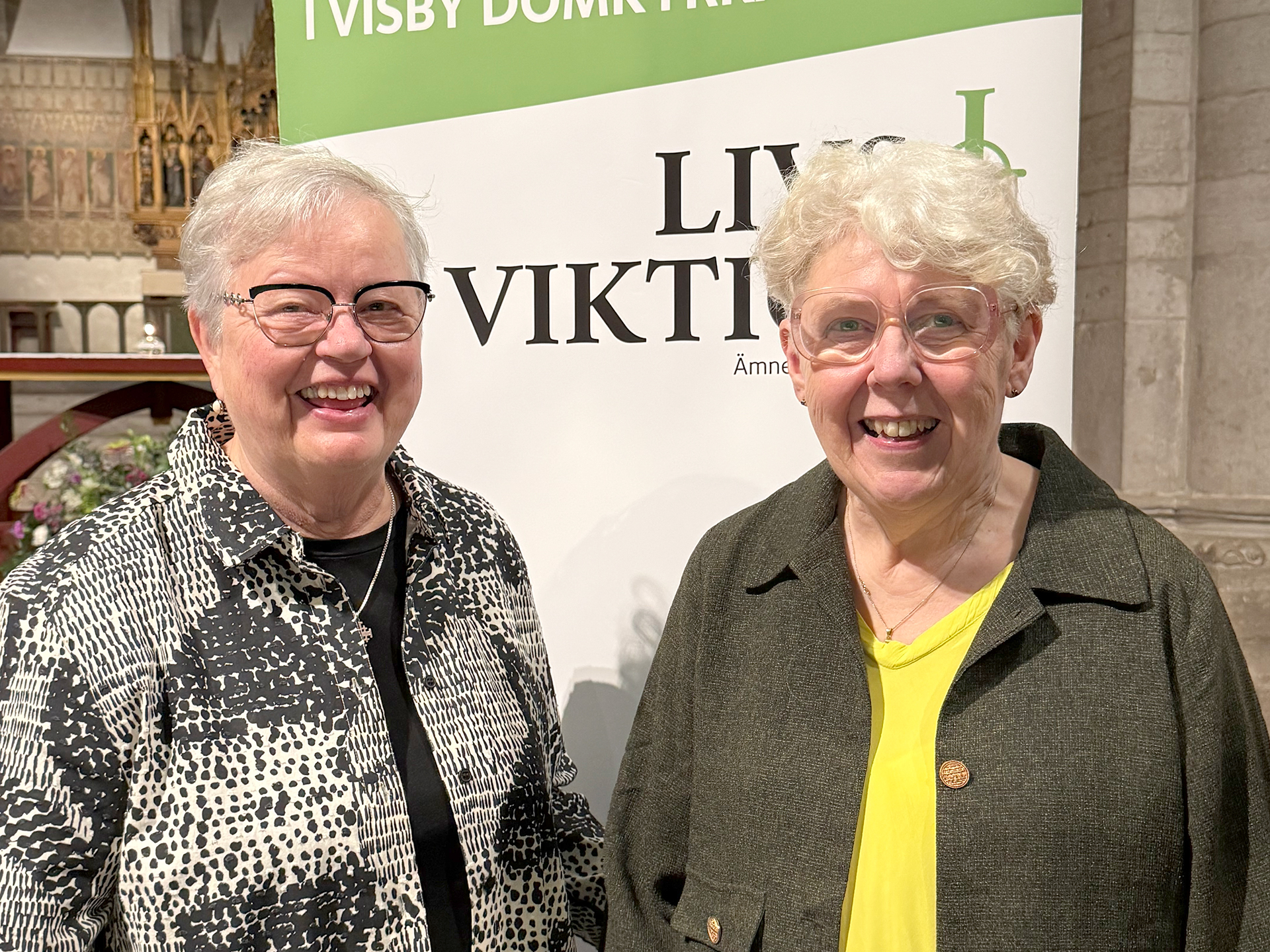 Två kvinnor i glasögon och vitt, kort hår framför en rollup