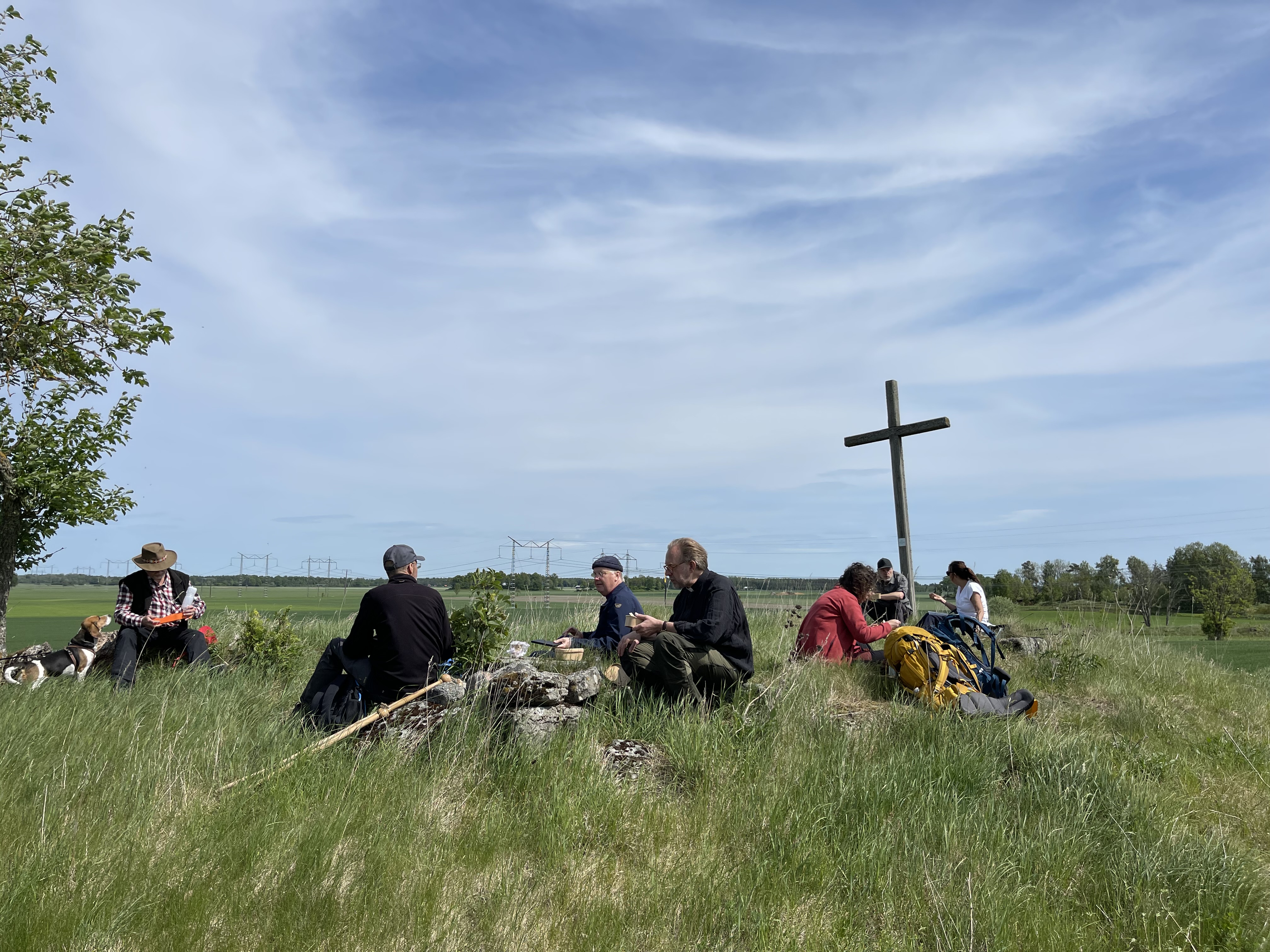 Pilgrimsvandrare äter lunch vid en gammal ruin invid ett träkors