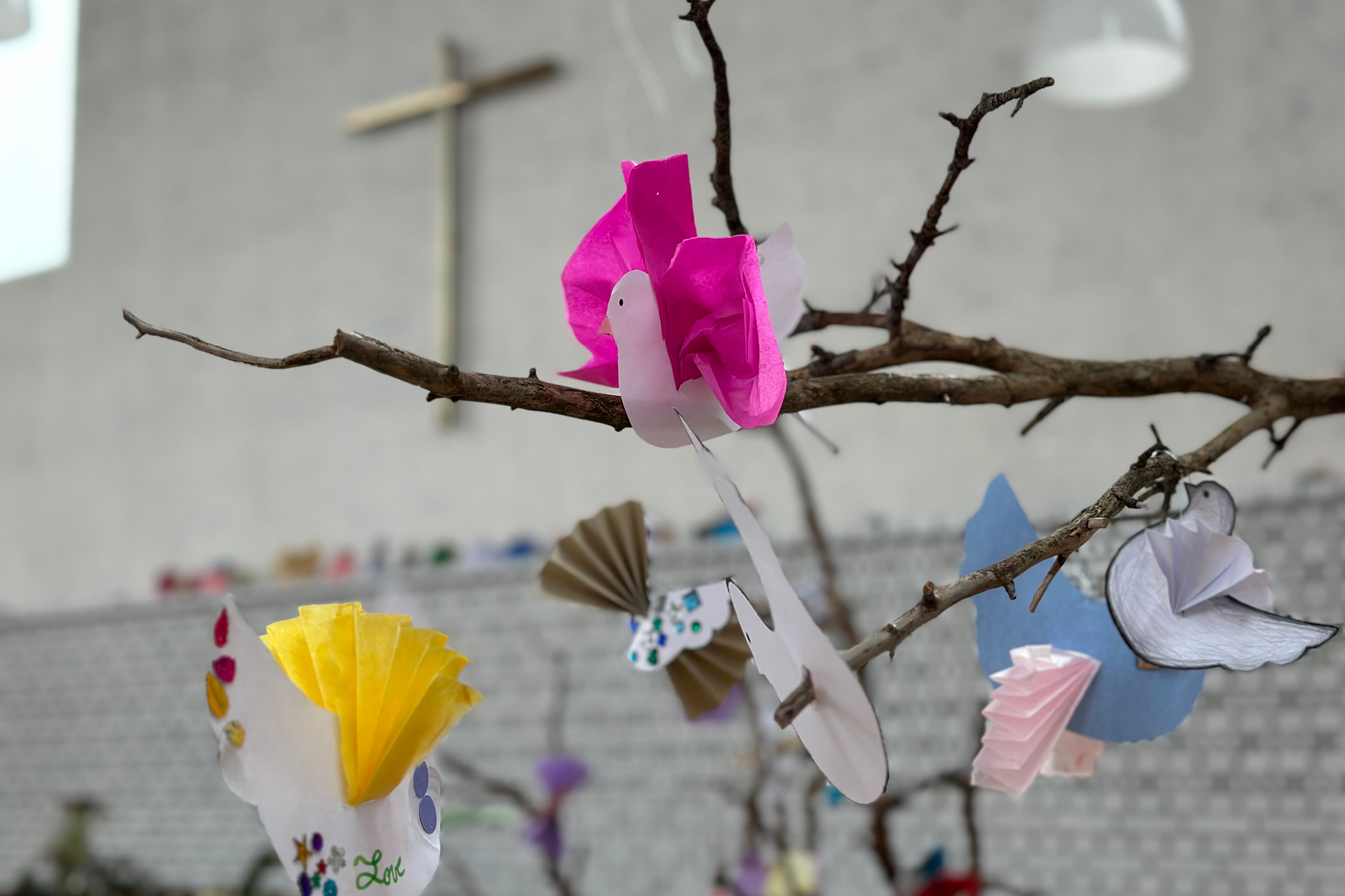 Pysslade fåglar på en gren framför korset i Årsta kyrka.