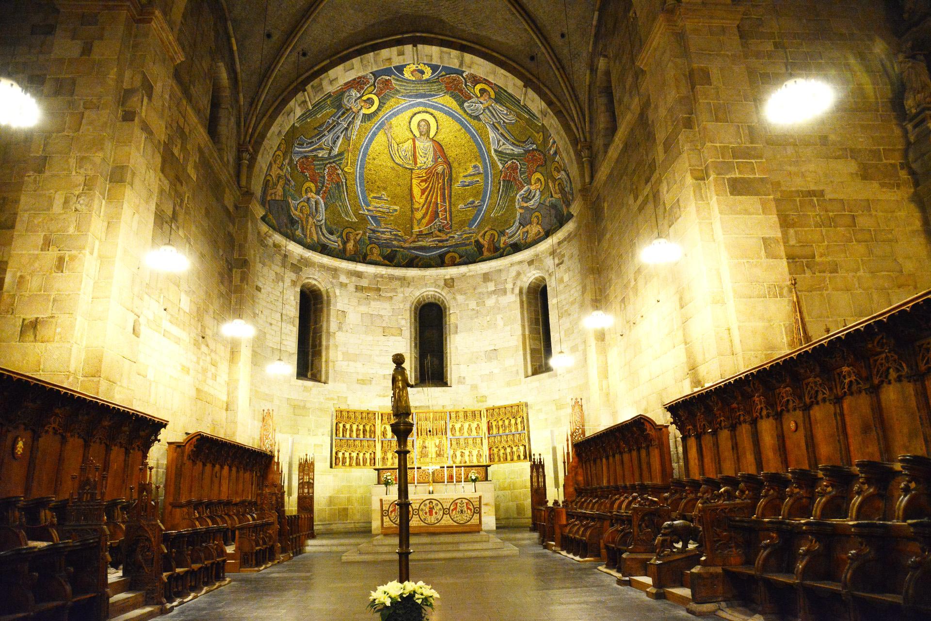 Högkoret med korstolar i mörkt trä, altare och kristusmosaik.