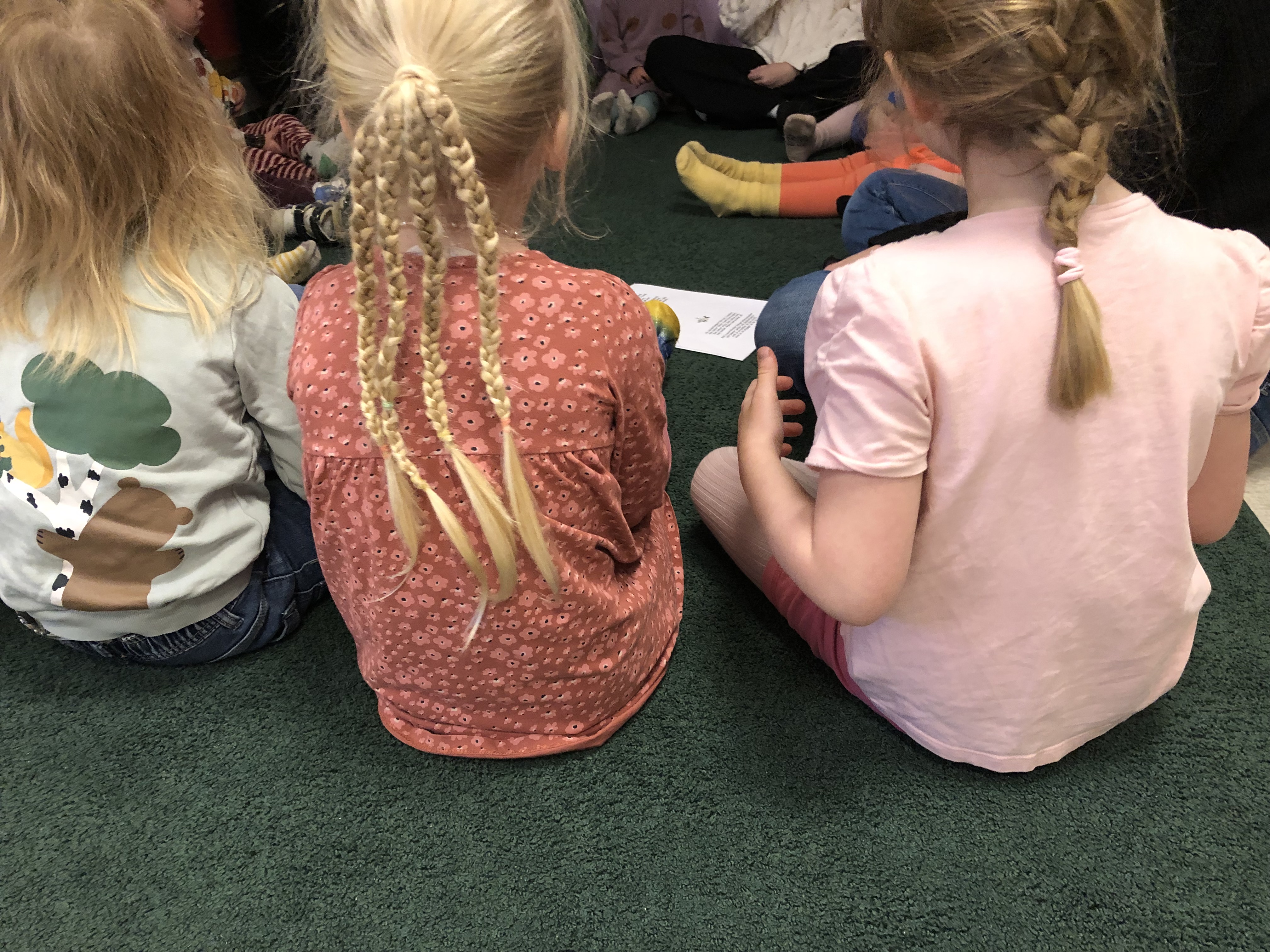 Barn med flätor i håret sitter i ring och sjunger.