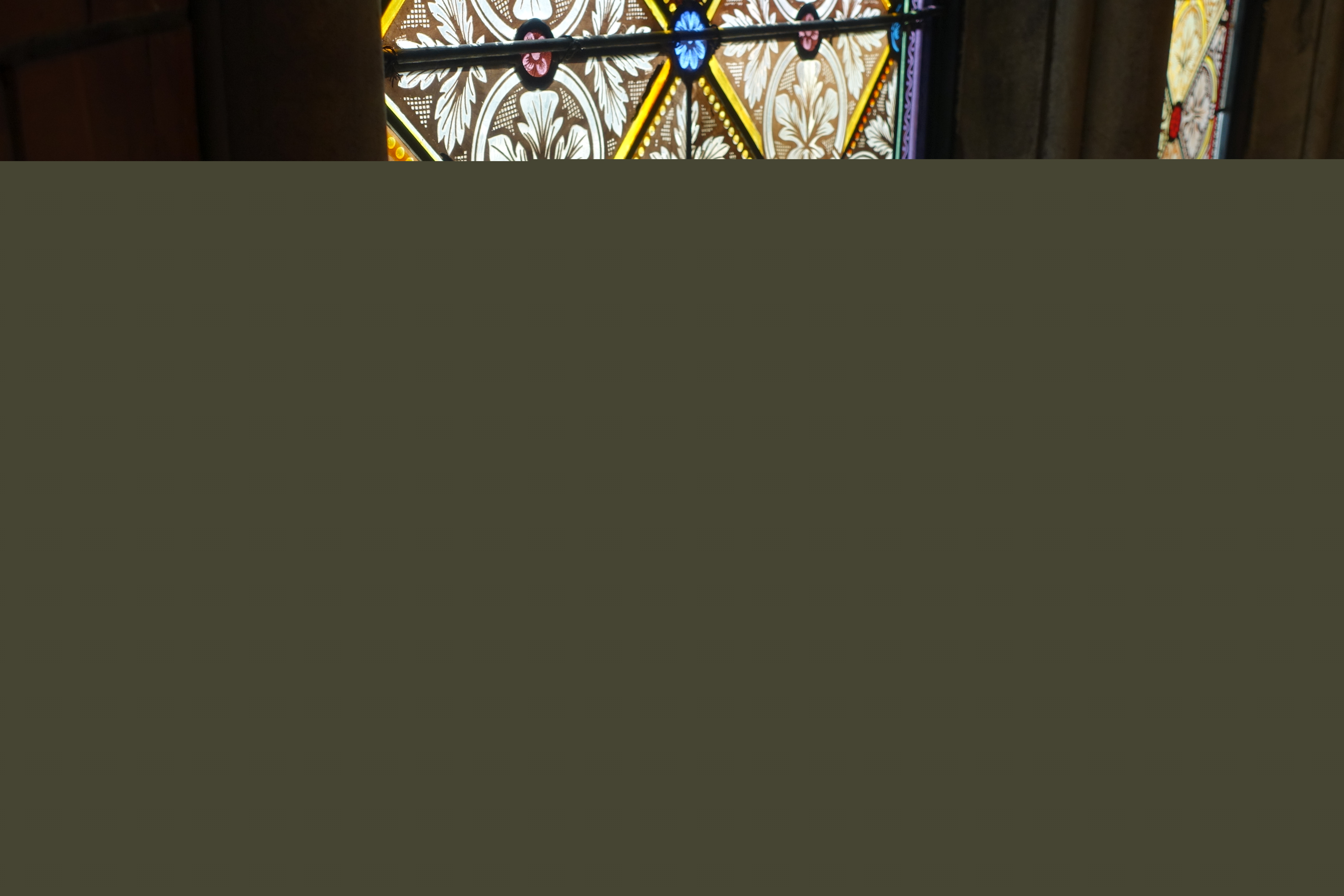 Solen lyser genom ett kyrkfönster och glasmålningarna reflekteras ner på fönsterkarmen och golvet