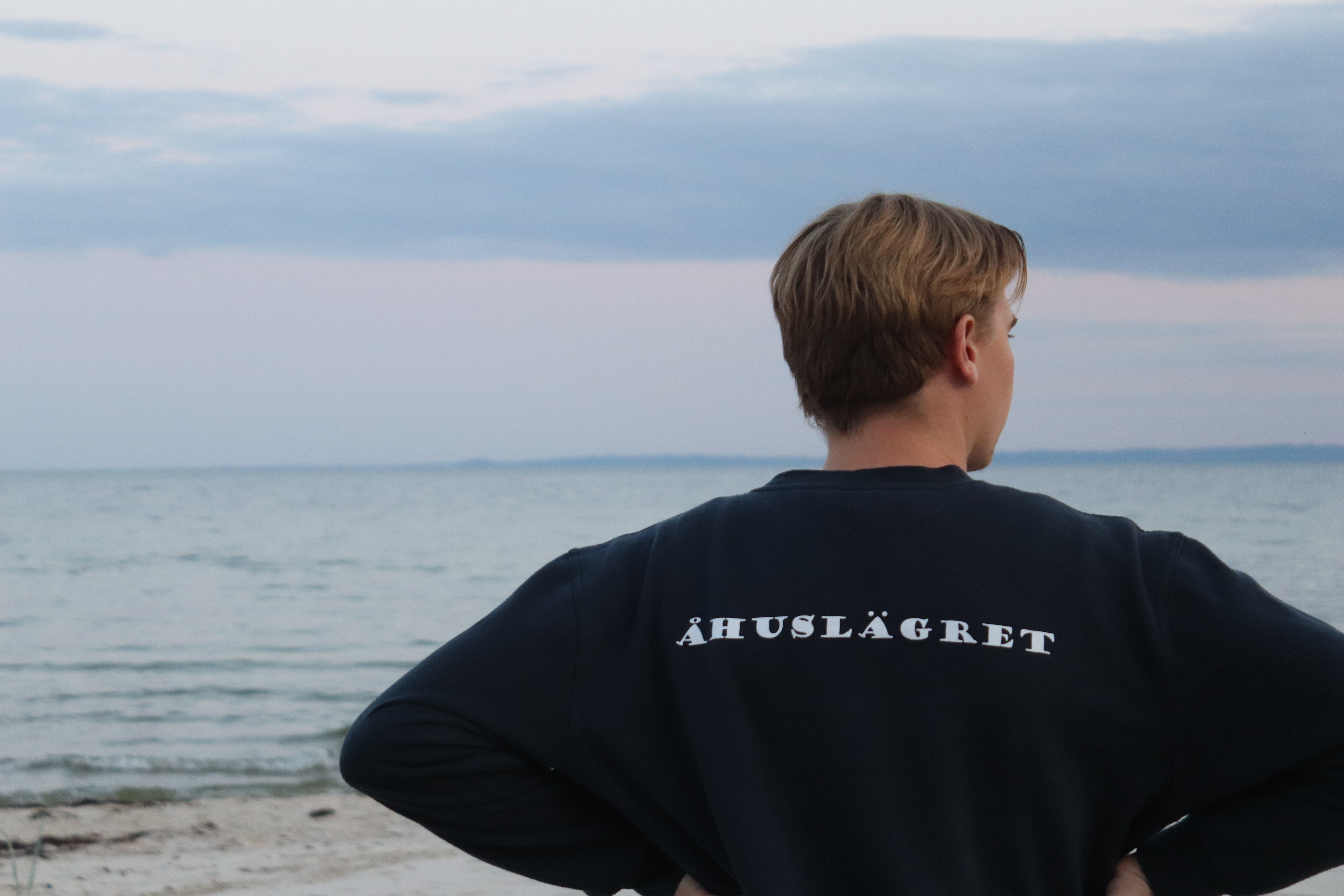 Man ser en person bakifrån i en blå tröja. På tröjans rygg står det Åhuslägret.