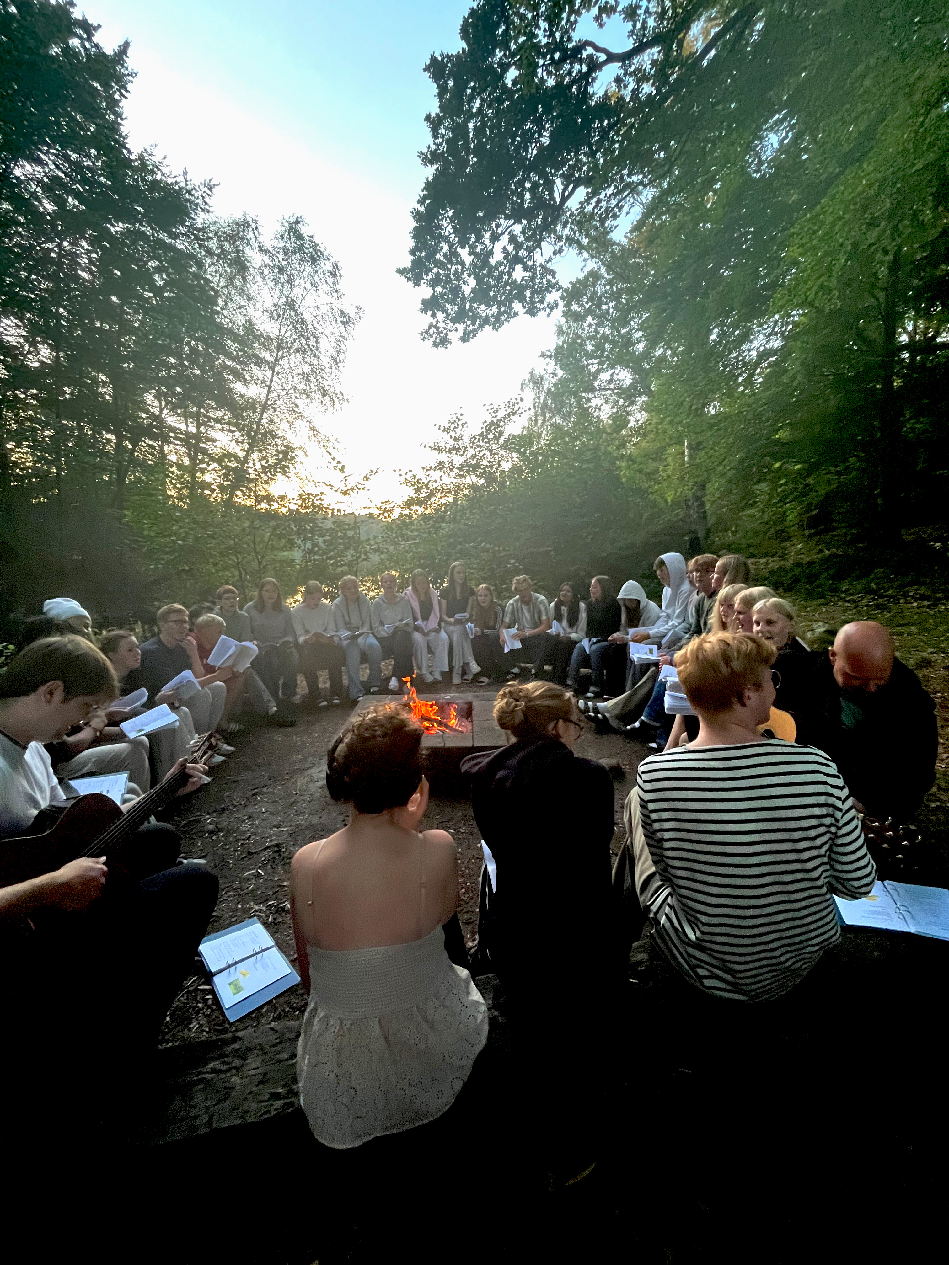 Man ser en konfirmandgrupp som sitter runt en brasa och sjunger.