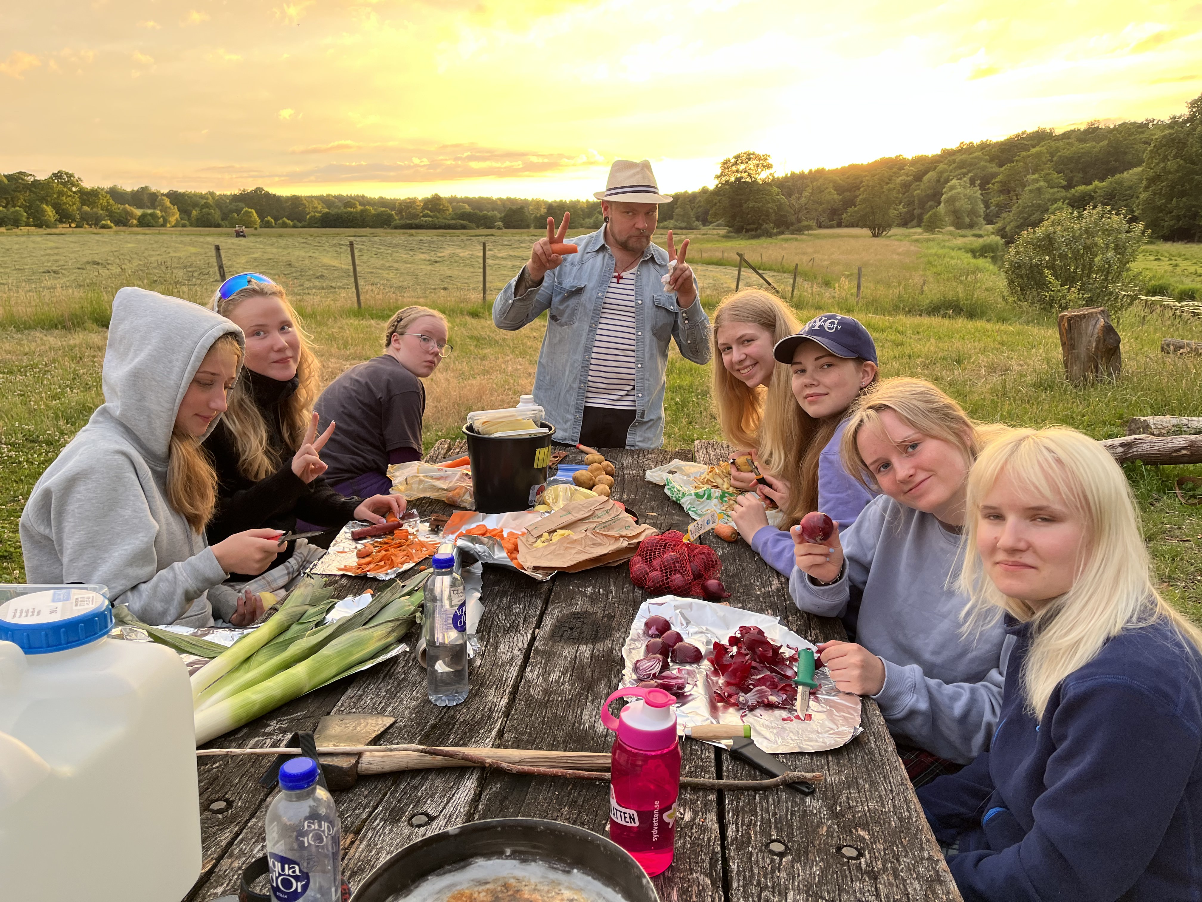 Ett gäng ungdomar sitter kring ett picknickbord ute i naturen och förbereder mat