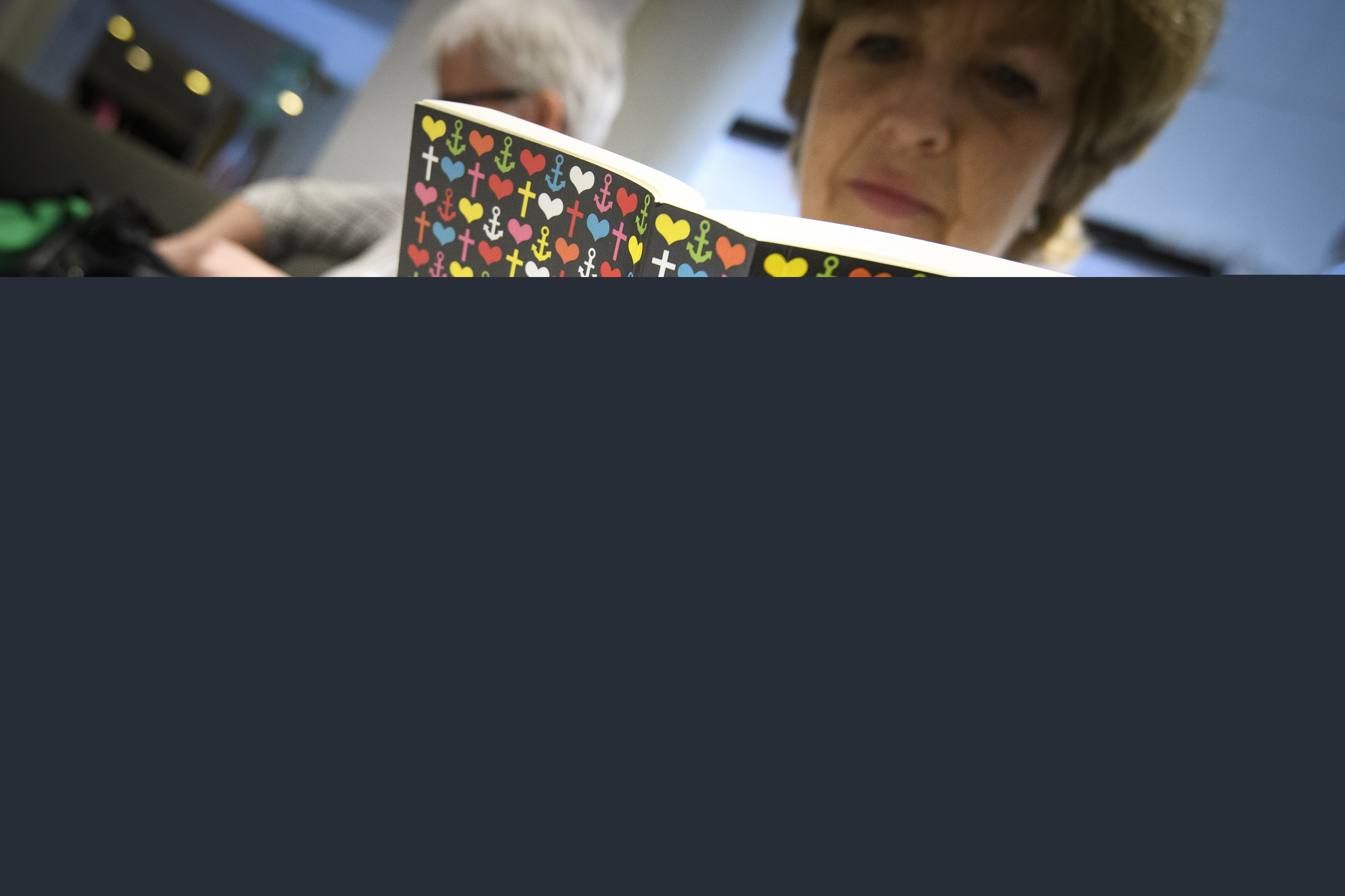 En kvinna sitter och läser Bibeln. I bakgrunden syns en kvinna till. 