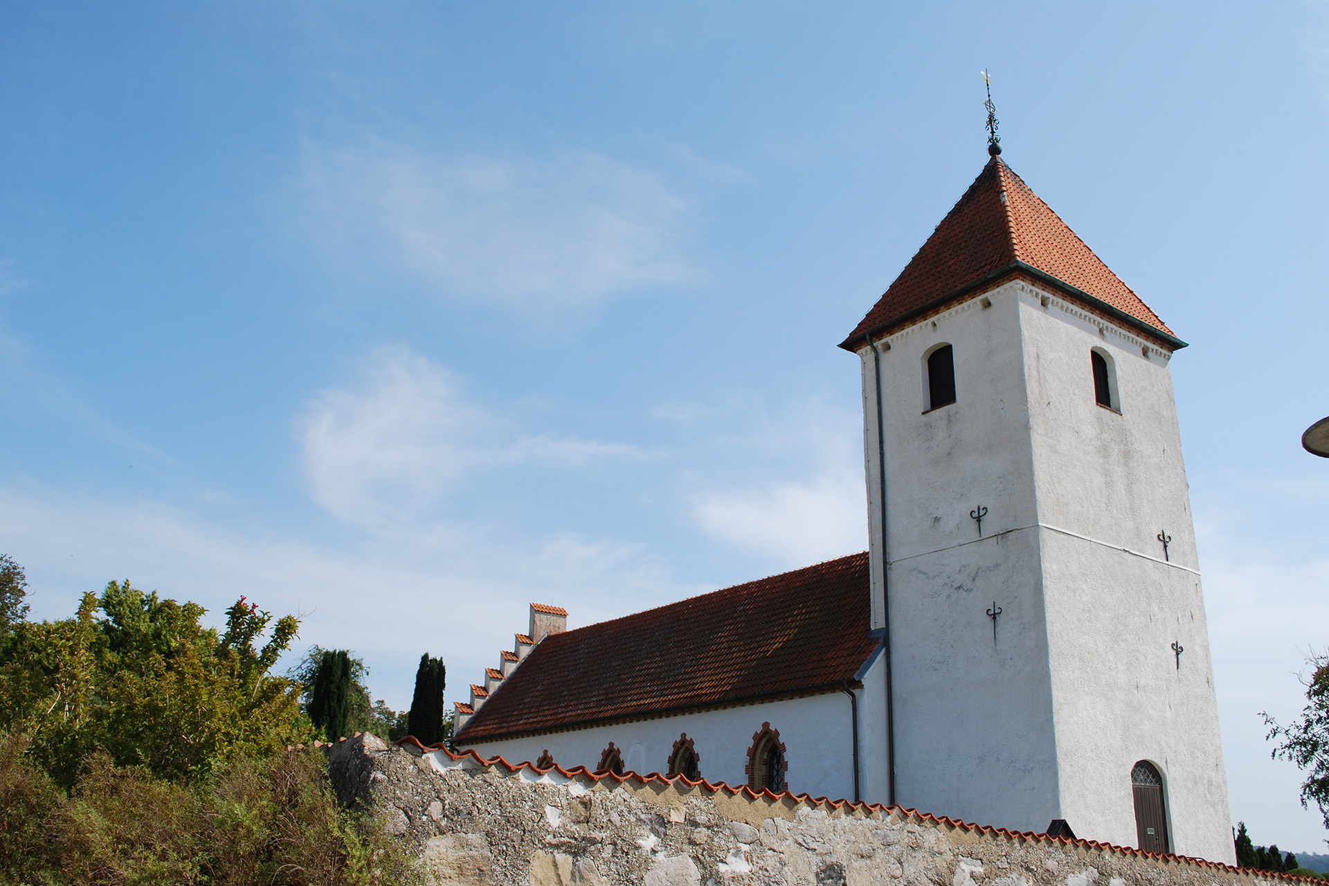 Vitkalkad kyrka mot blå himmel i solsken. En låg stenmur syns i nederkanten av bilden.