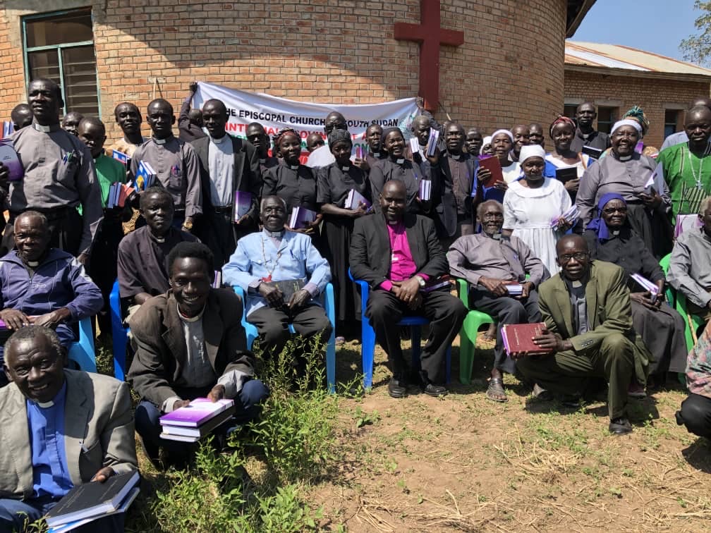 Personer sitter och står framför en byggnad med ett kors på väggen.