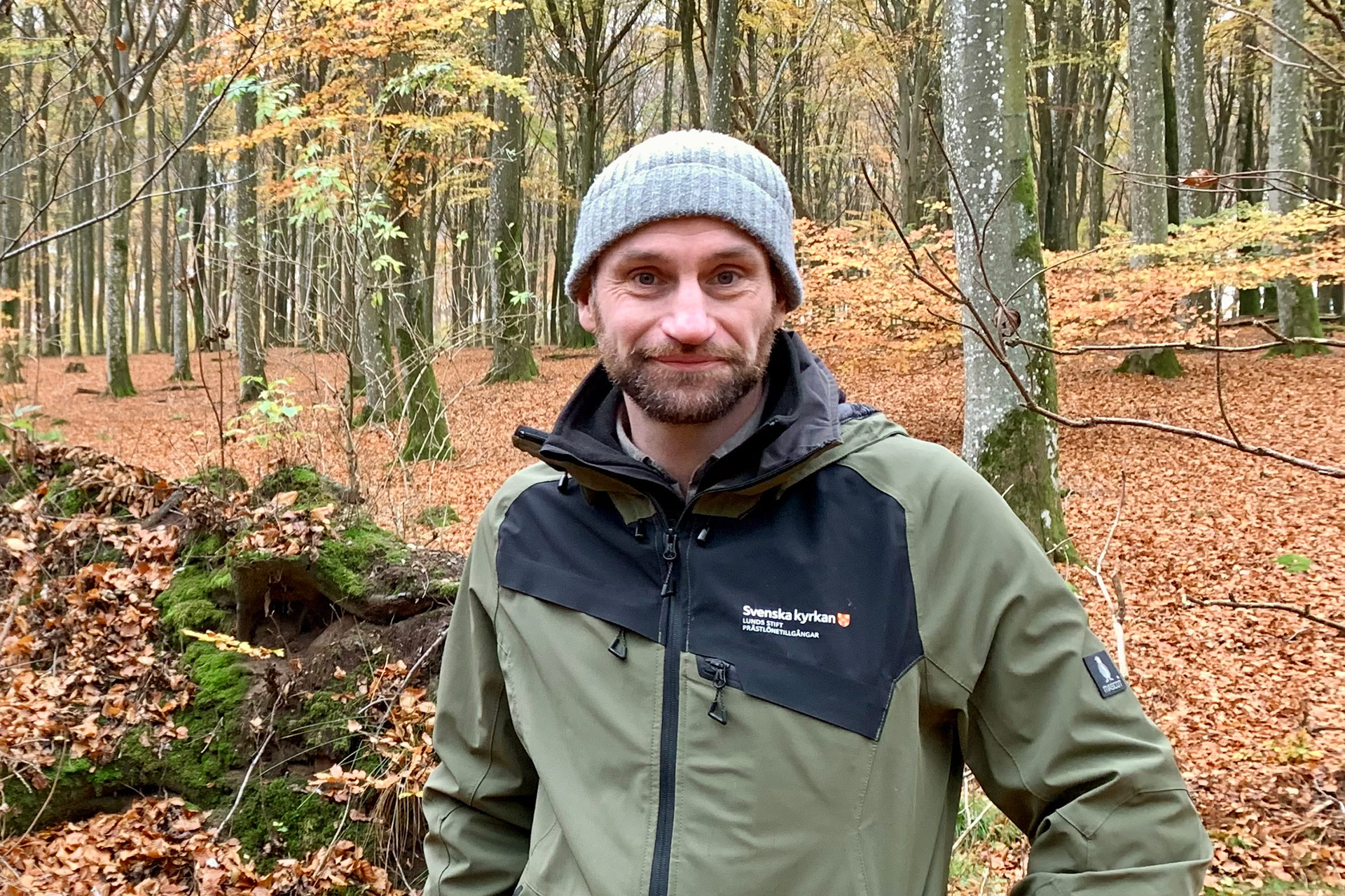 Man i friluftskläder står i en höstlik bokskog.