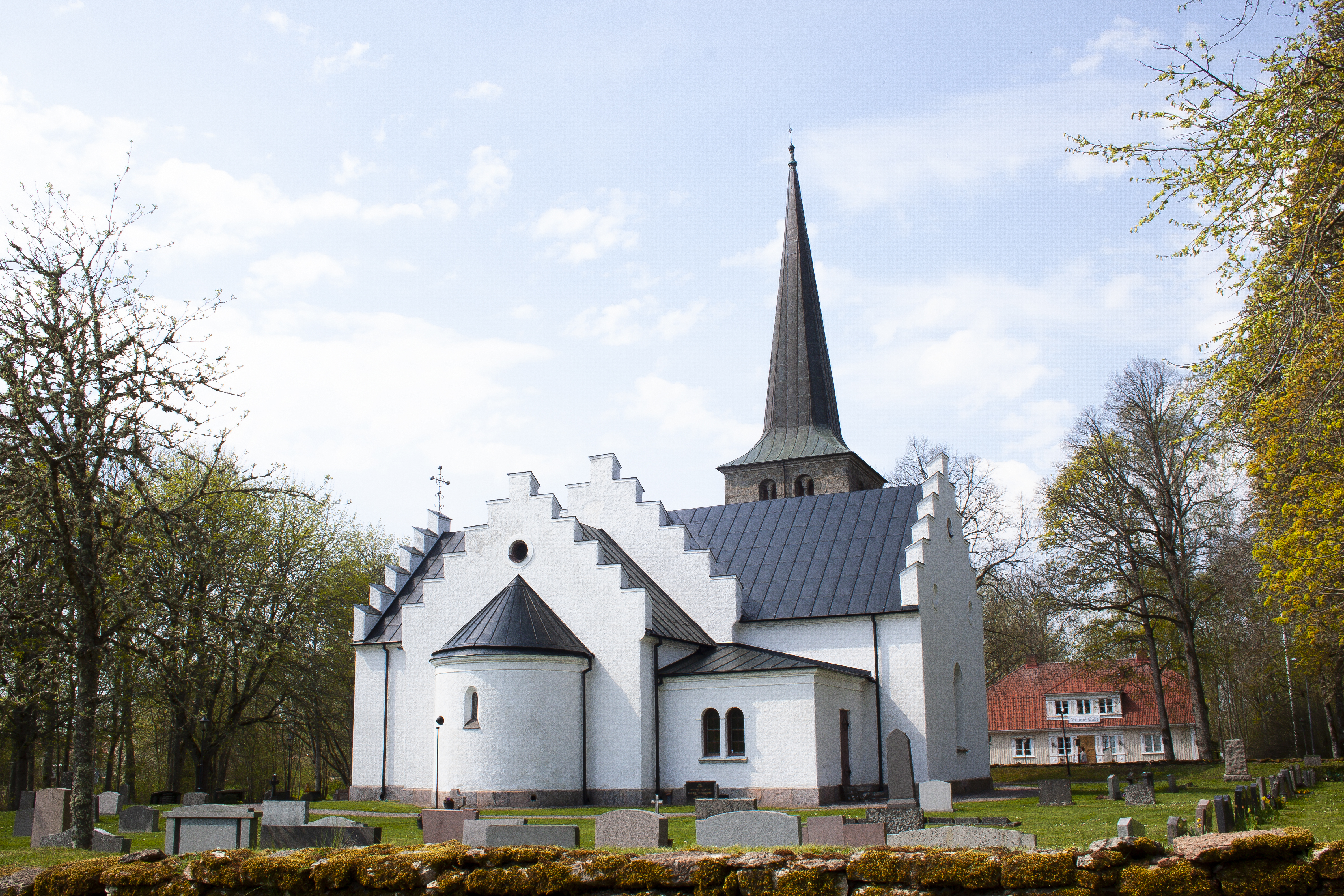 Valstads kyrka sett bakifrån, runt omkring är det gröna träd och grönt gräs på marken samt en mur som omger kyrkan.