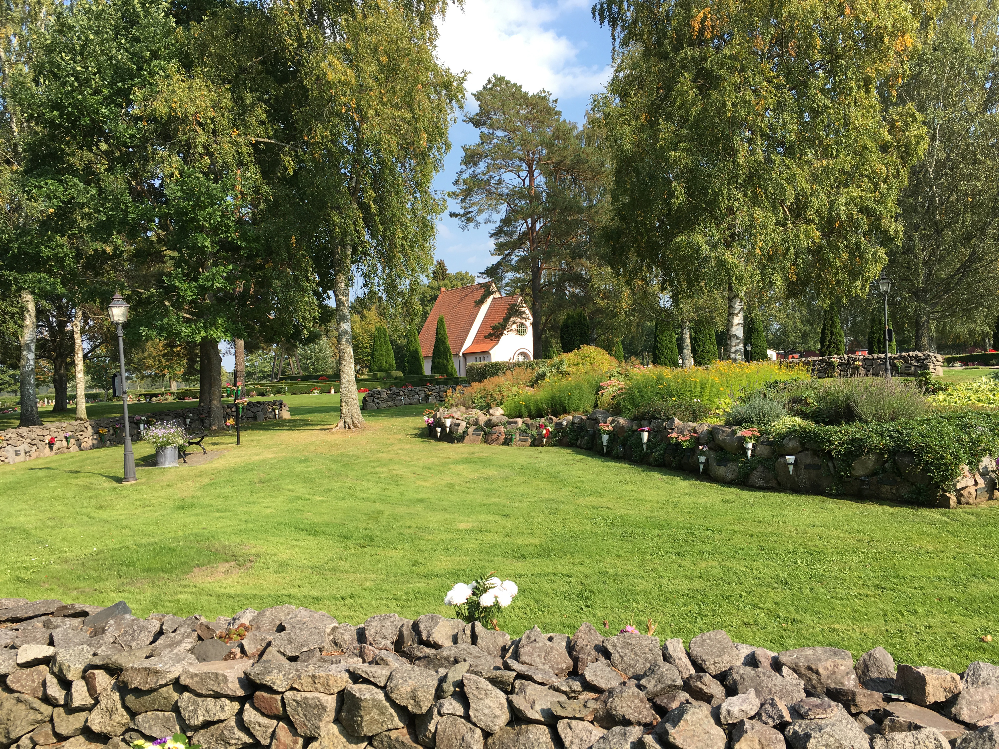 Kyrkogård med ett kapell långt bort i bakgrunden, i förgrunden syns en del av en stenmur.
