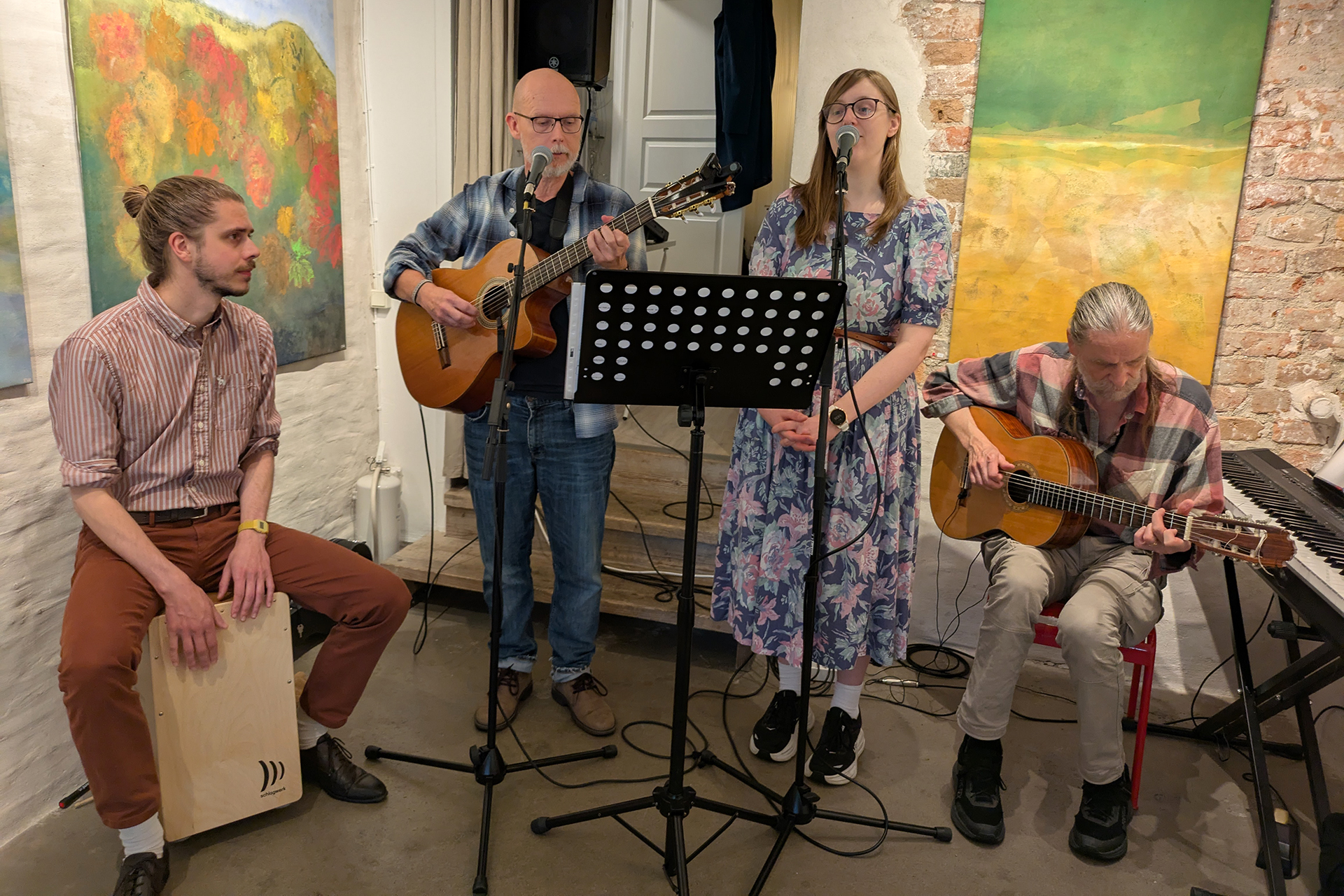 Bandet Grannar, fyra medlemmar med gitarrer, slagverk och mikrofon, sjunger ochs pelar uppställda kring ett notställ i ett ganska trångt rum med färgglad konst på väggarna. Det är tre män och en kvinna.