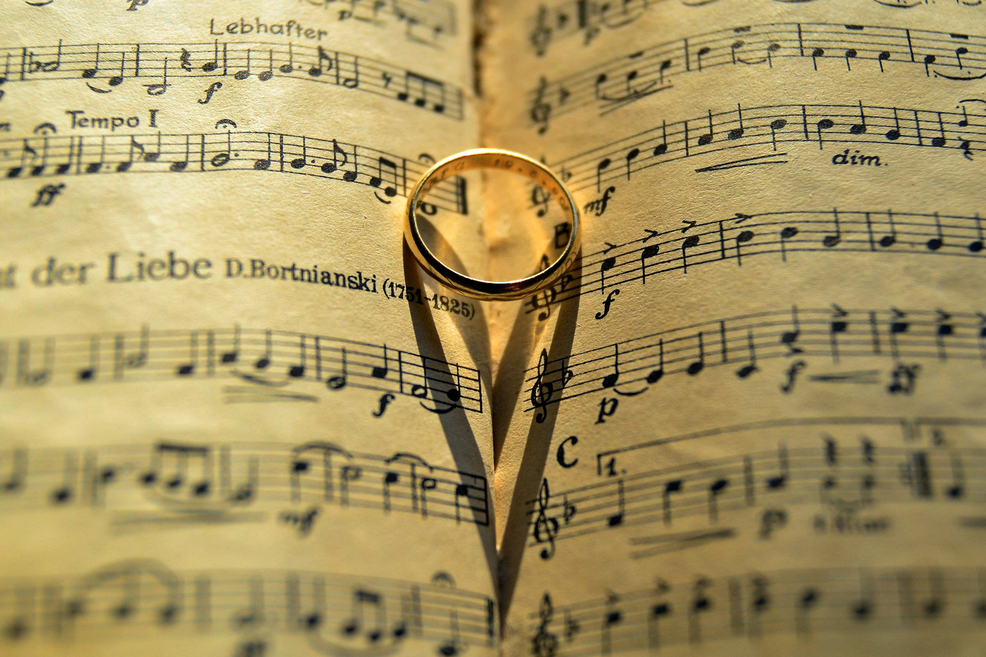 En vigselring ligger på notblad och skuggorna från ringen bildar ett hjärta.