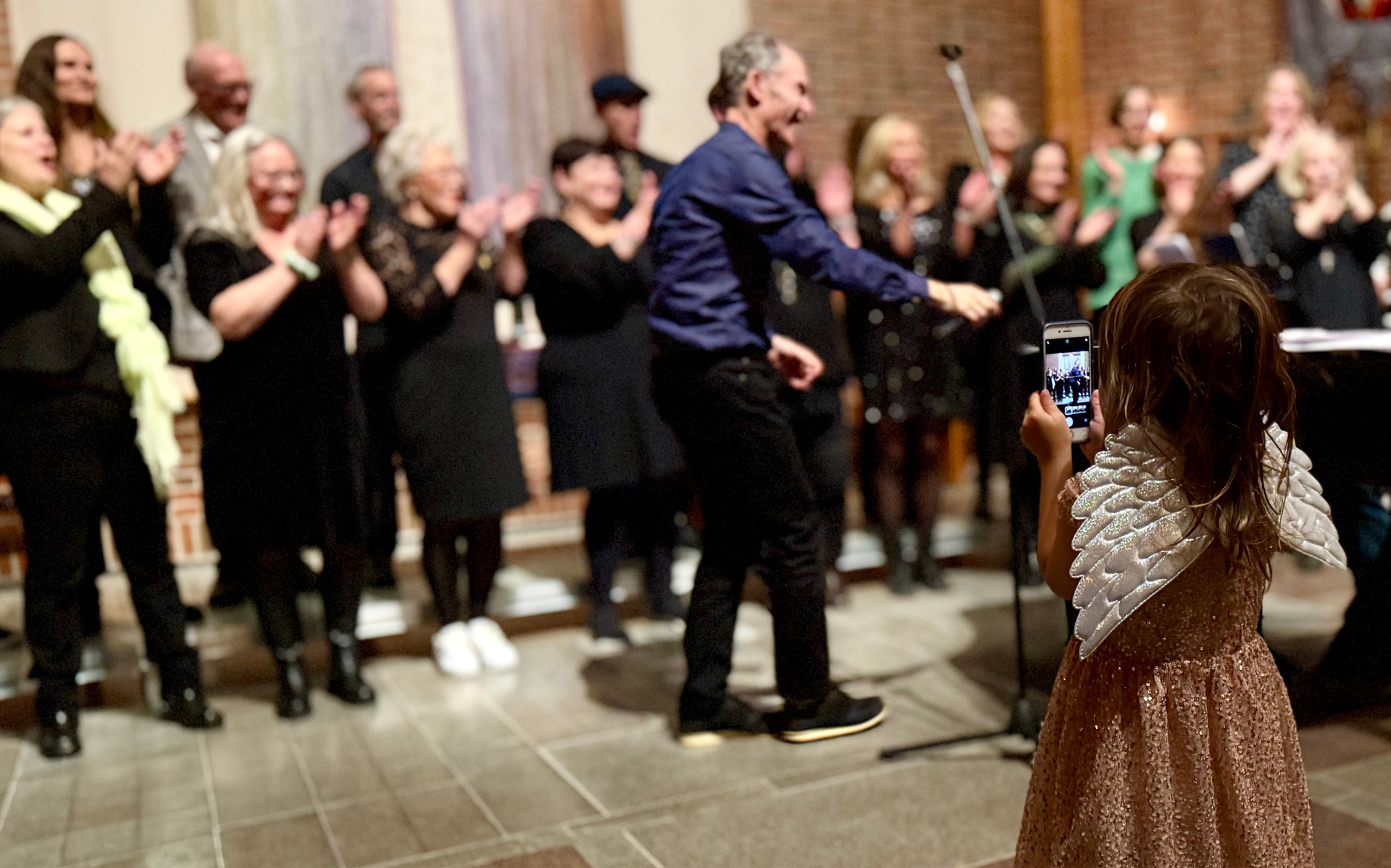 En kör står uppställda för konsert. En flicka tar en bild med sin mobiltelefon.