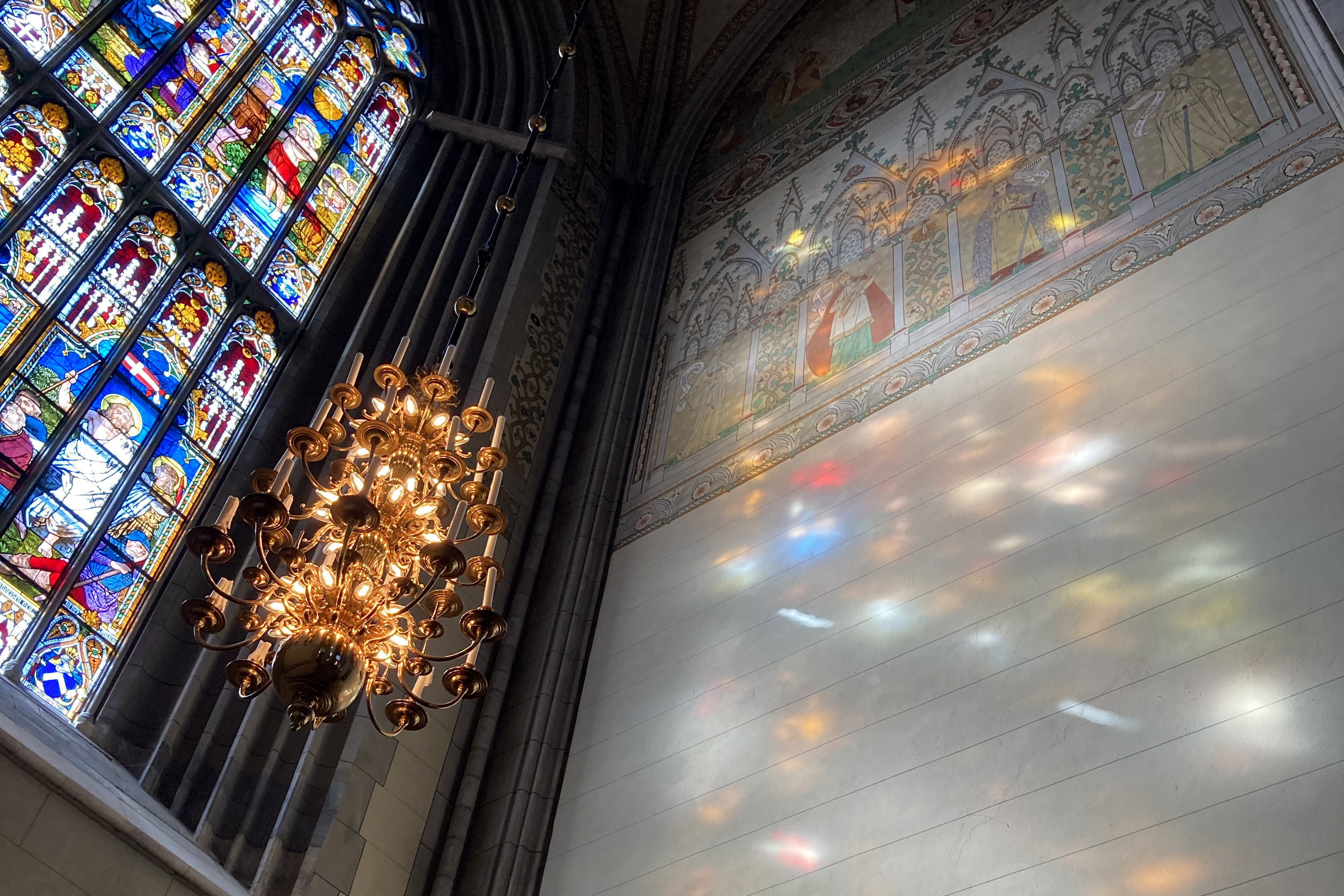 Domkyrkans södra fönsters målningar avspeglar sig i klara färger i solreflexerna på södra korets vägg.