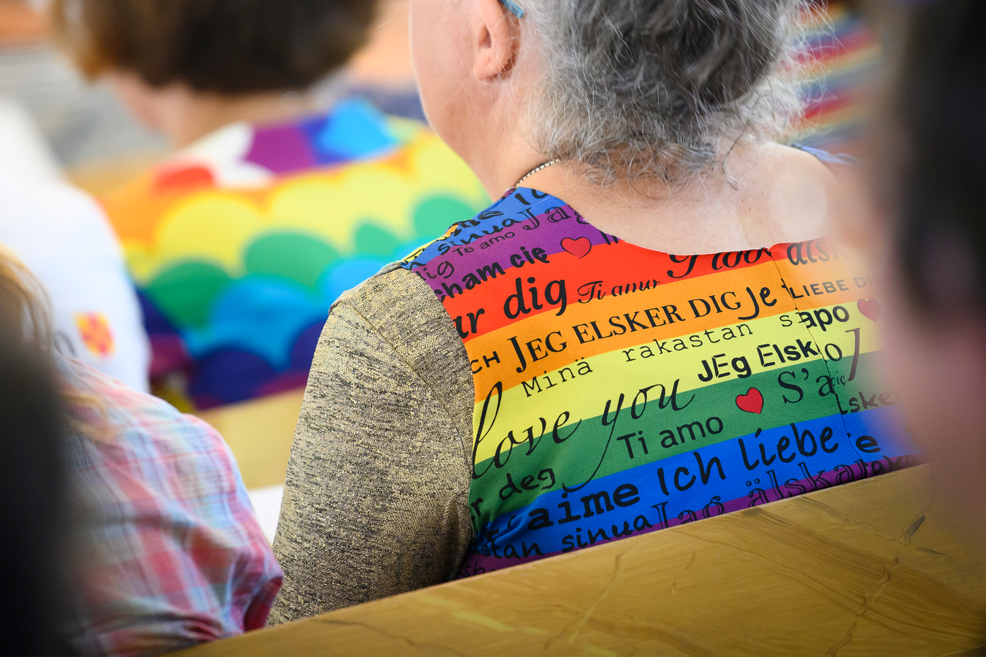 En person med en väst i regnbågsfärger. På västen står det "Jag älskar dig" på flera olika språk.