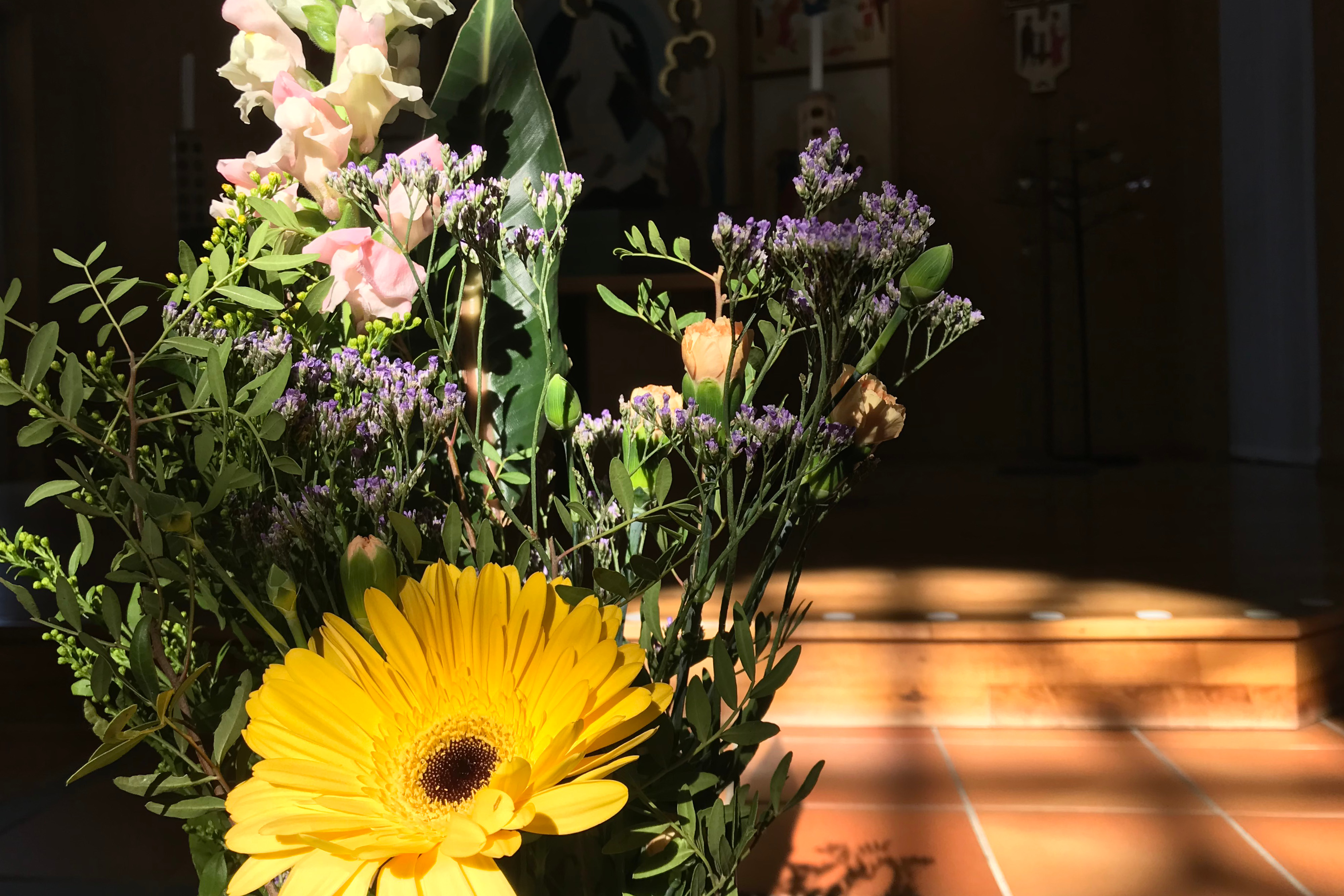 Bukett av blandade sommarblommor belysta av kvällssolen, siluett av ett solkors syns på golvet bakom.