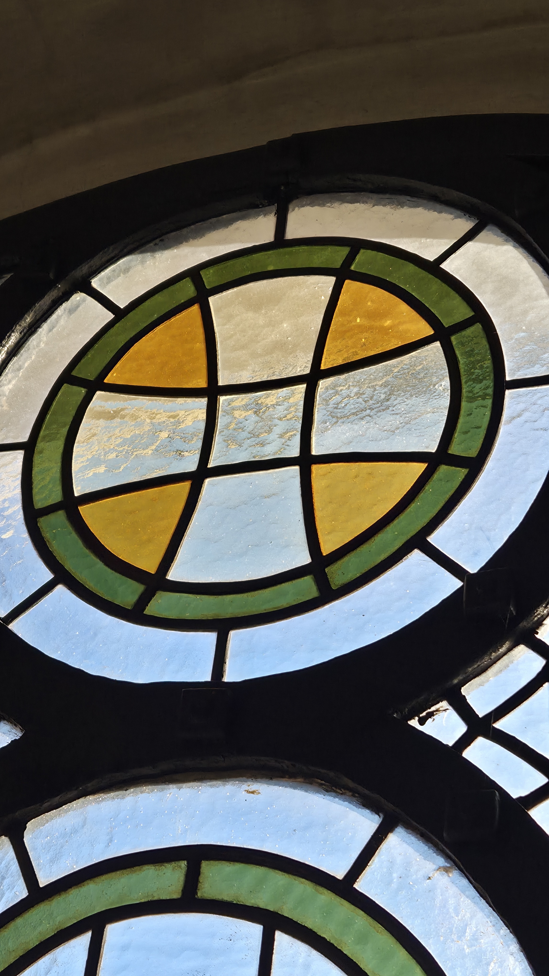 Bit av ett kyrkfönster, glasrutorna bildar ett kors i en grön ring.