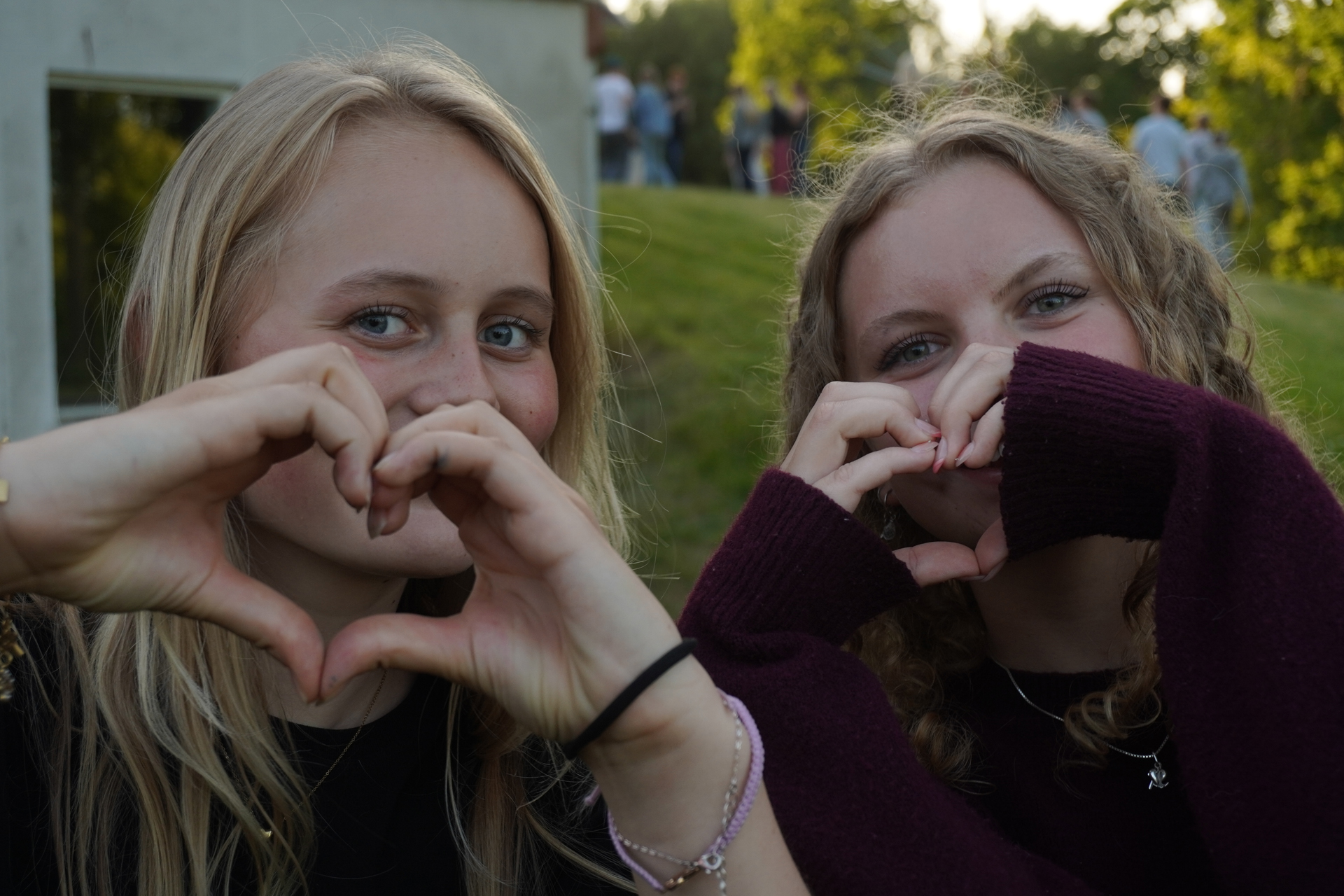 Två tjejer står utomhus och formar sina händer till hjärtan framför sina ansikten.