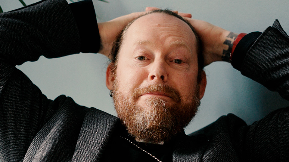 Prästen Johan Husberg lutar sig tillbaka i en soffa och lägger händerna bakom huvudet