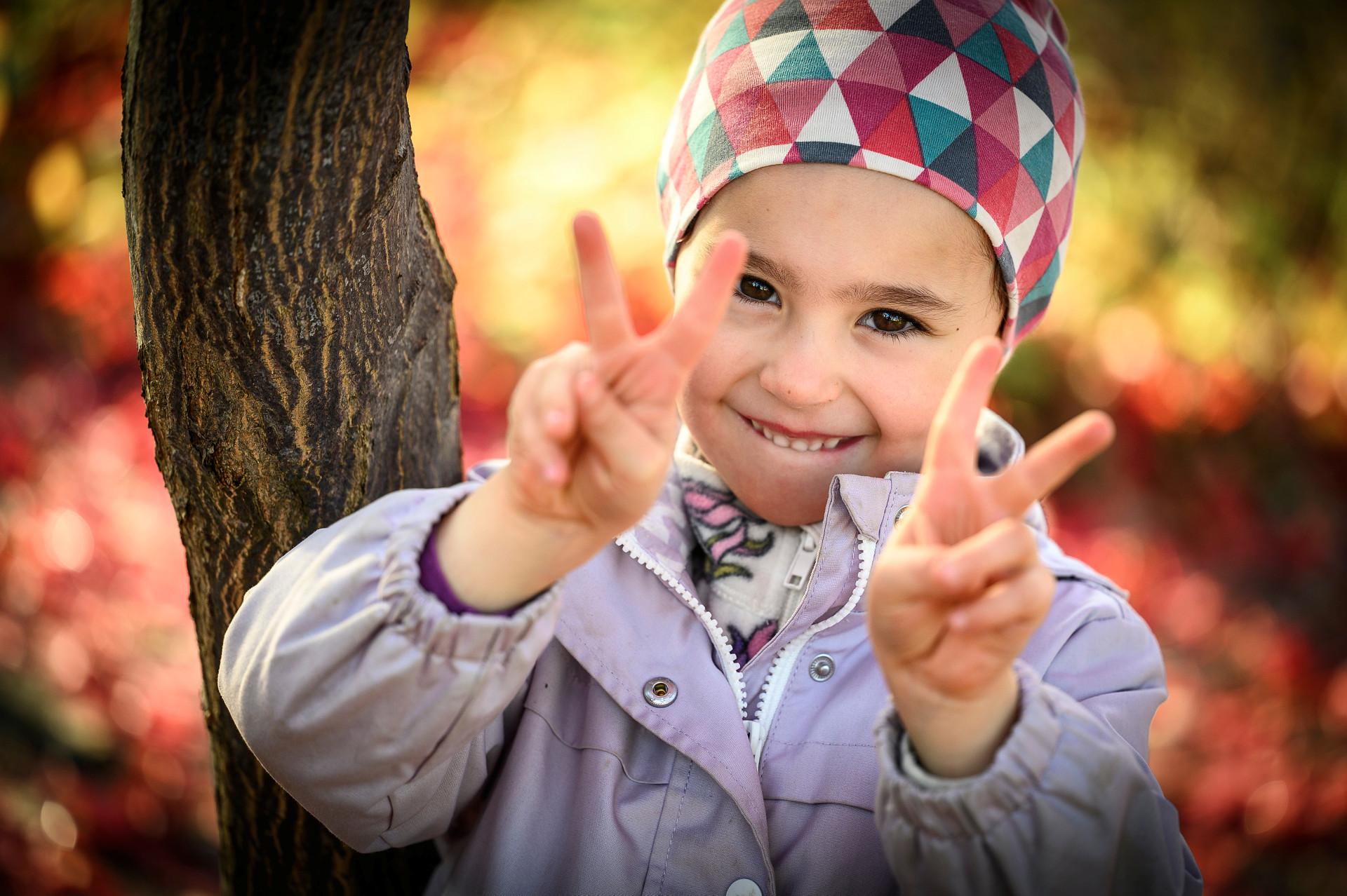Ett glatt barn med rutig mössa gör V-tecknet med båda händerna mot kameran.