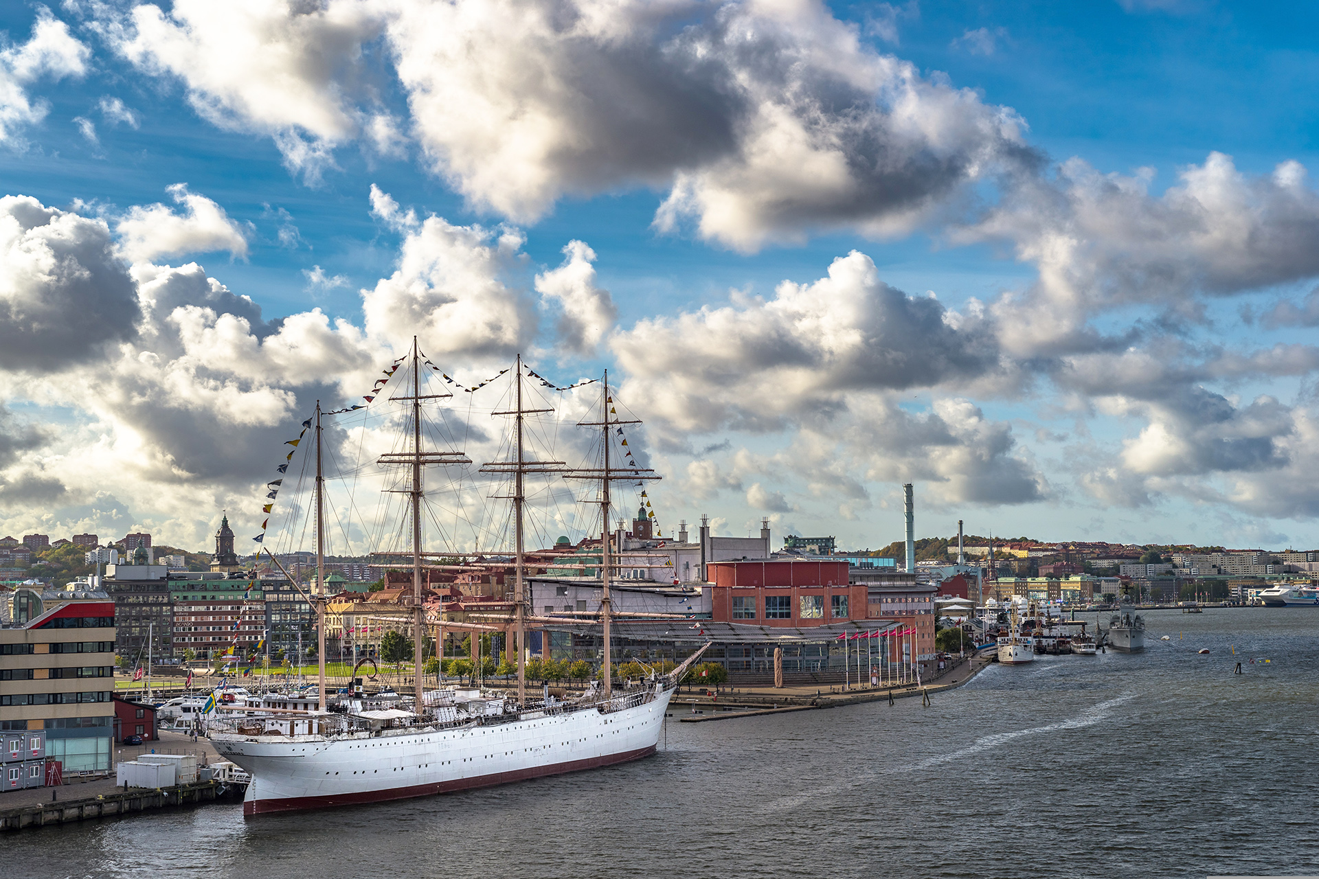 Vy över älv, fartyg och byggnader. Moln på blå himmel.