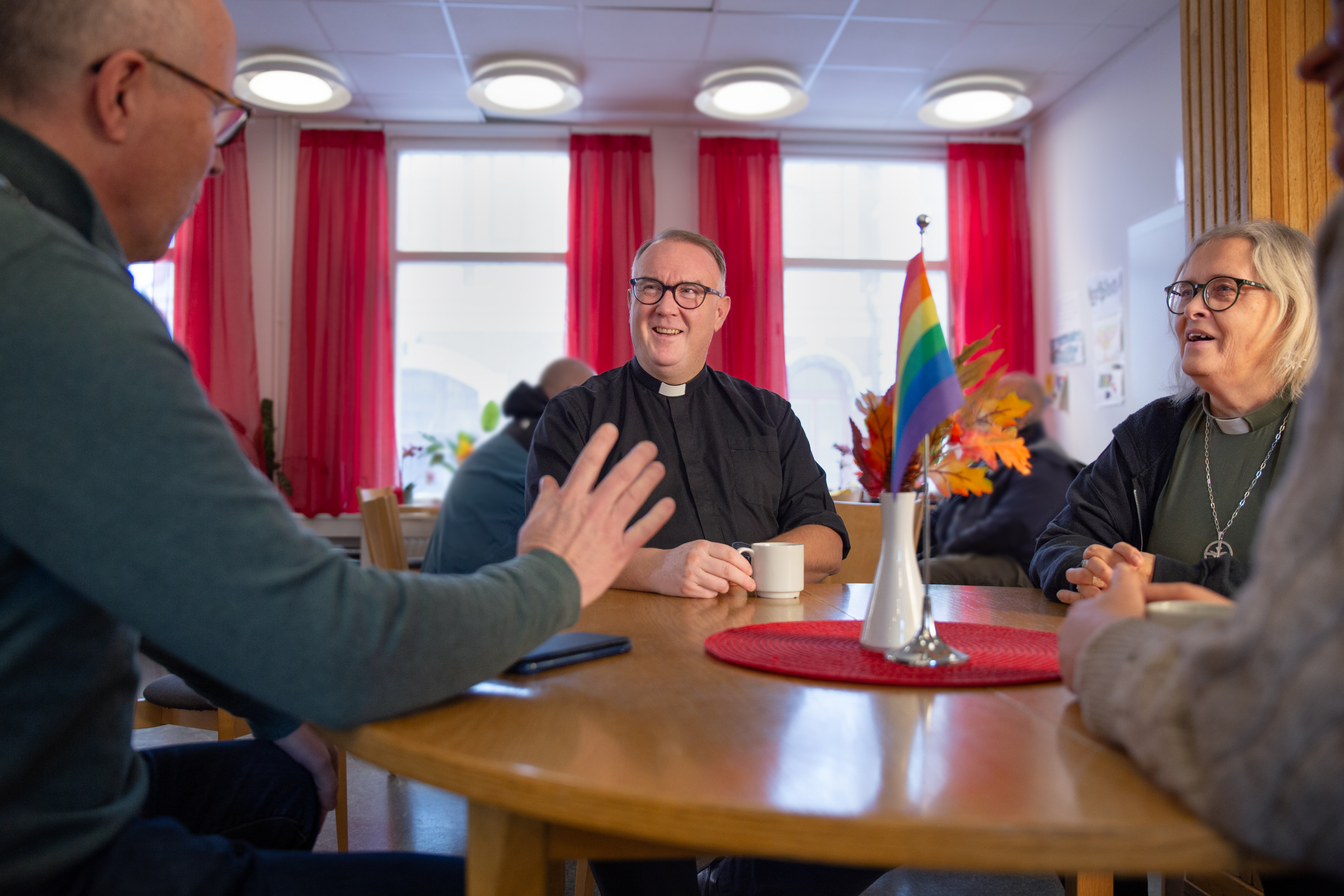 En domprost sitter vid ett bord med andra diakoner och samtalar