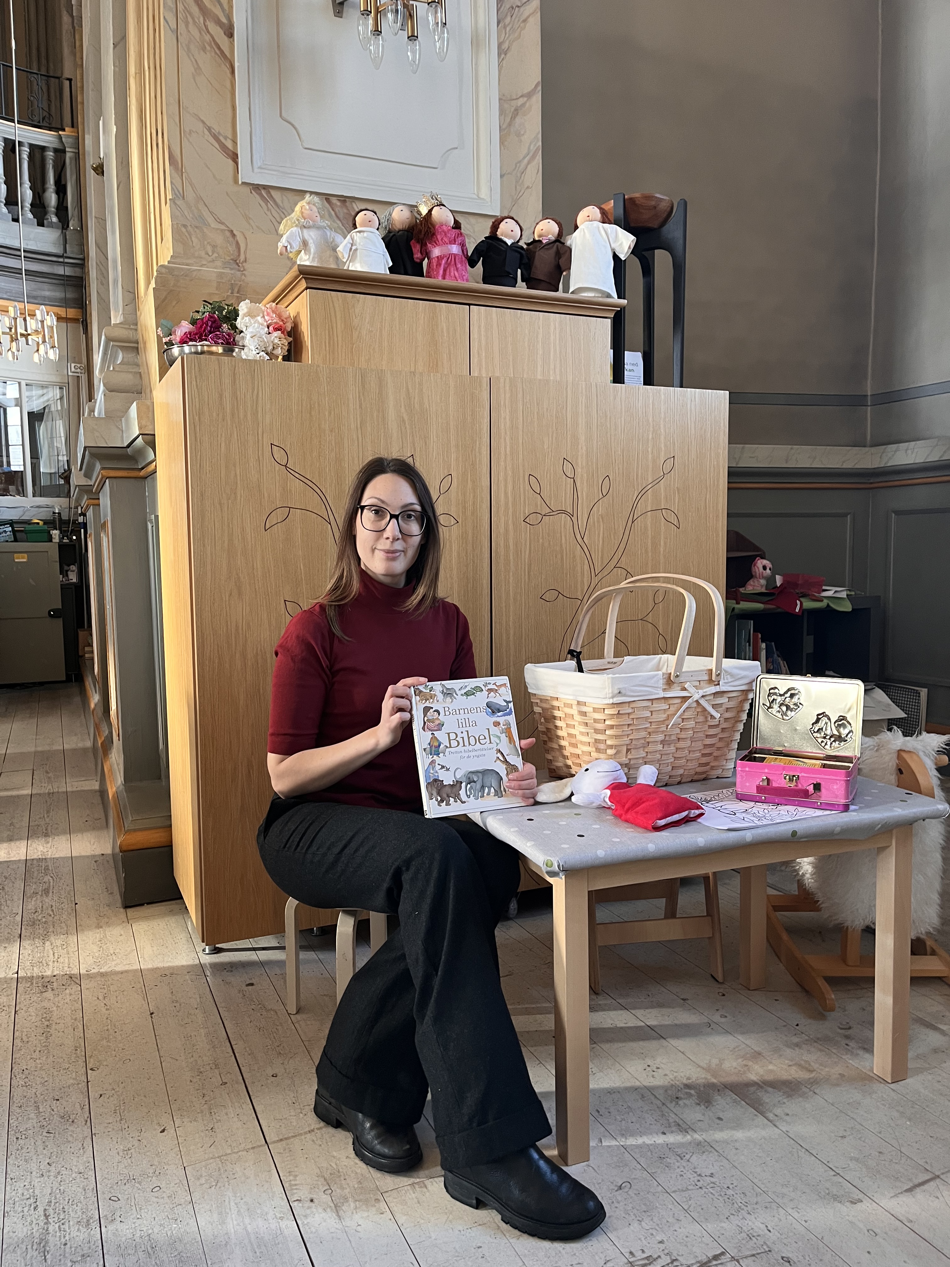 Kvinna sitter med boken Barnens bibel framför Barnens altarskåp i Vaxholms kyrka.
