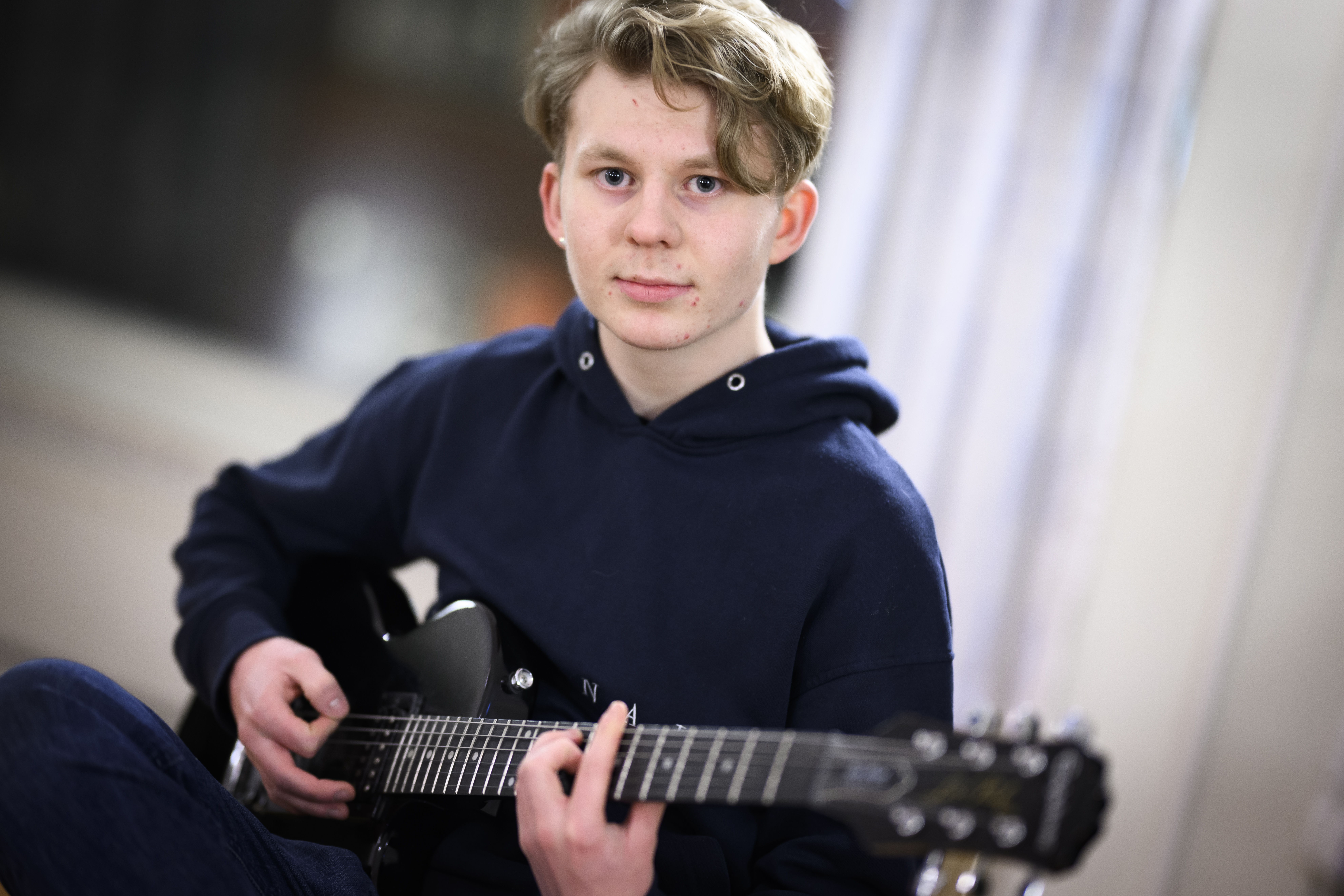 En ung kille sitter med en svart elgitarr i knät.